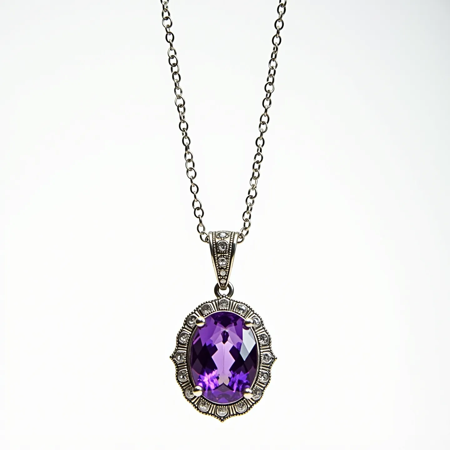 This amethyst necklace features a striking oval-cut amethyst gemstone, prominently set in a detailed silver setting that enhances its vibrant purple hue. The setting, adorned with intricate decorative elements, securely holds the gemstone with four prongs. The pendant is attached to a silver chain with an elegant design, possibly made of stainless steel or sterling silver, enhancing its durability and aesthetic appeal. A decorative bail seamlessly connects the pendant to the chain, providing a cohesive and stylish look. The necklace likely features a simple clasp mechanism to ensure easy and secure wearability.