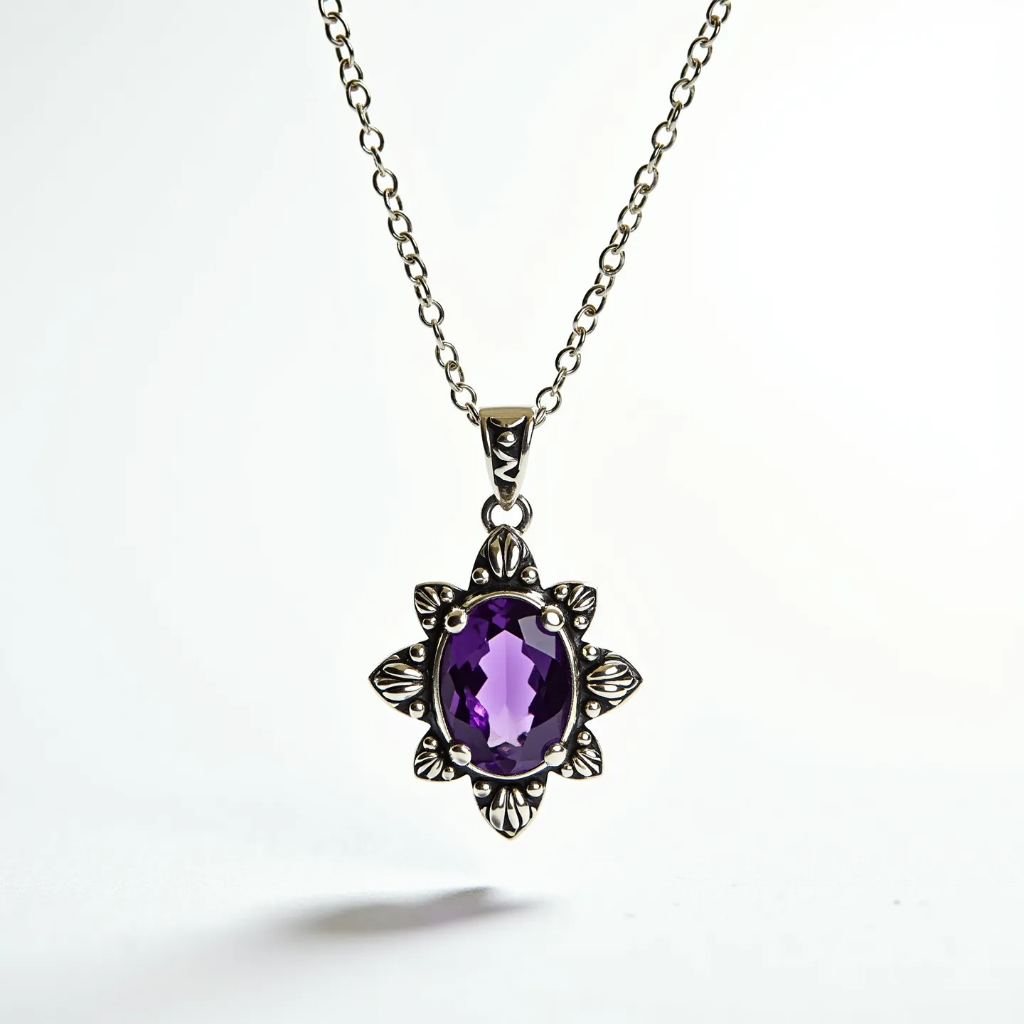 This amethyst necklace features a pendant with an oval-cut amethyst stone set in an intricate decorative metal setting, which appears to be silver. The design surrounding the stone includes ornate detailing that resembles floral or leaf motifs, adding a touch of elegance and sophistication. The pendant is suspended from a classic chain that complements its style, often linked to provide both durability and a graceful appearance. The clasp used in this necklace likely provides secure attachment and ease of use, though it's not visible in the image. Overall, the necklace has a refined and timeless aesthetic, highlighting the beauty of the amethyst stone.