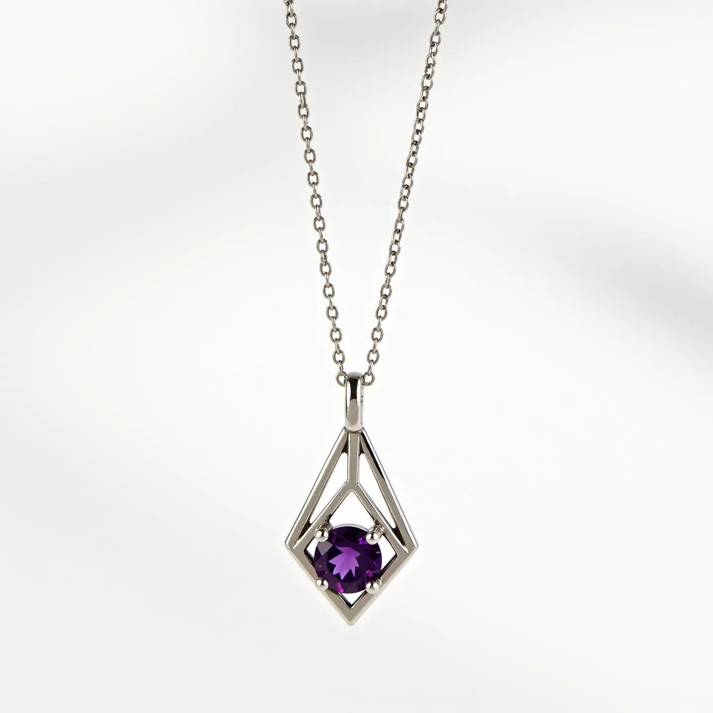 This amethyst necklace features a striking geometric pendant design crafted from what appears to be a lustrous metal, likely silver or white gold. At the center of the pendant is a round-cut amethyst, securely held in place by a four-prong setting, showcasing the stone's deep purple hue. The pendant's open framework complements the vivid gemstone, adding a modern yet elegant touch to the piece. It is suspended from a delicate chain that is possibly made of the same metal as the pendant, offering an understated and cohesive look. The chain is finished with a standard clasp, ensuring both functionality and security.