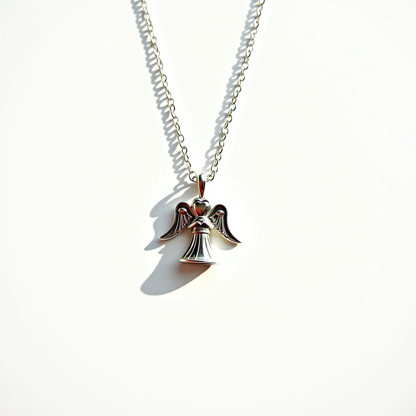 This angel necklace features a simple yet elegant design, crafted from polished silver. The pendant showcases an angel with detailed wings, a flowing robe, and a heart shape near the top, emphasizing its celestial theme. The chain itself is composed of interlocking links, creating a delicate and refined appearance. There are no visible gemstones or additional embellishments on the pendant. The necklace is likely secured with a standard lobster clasp, ensuring ease of wear and security. Overall, this piece exhibits a classic and understated charm.