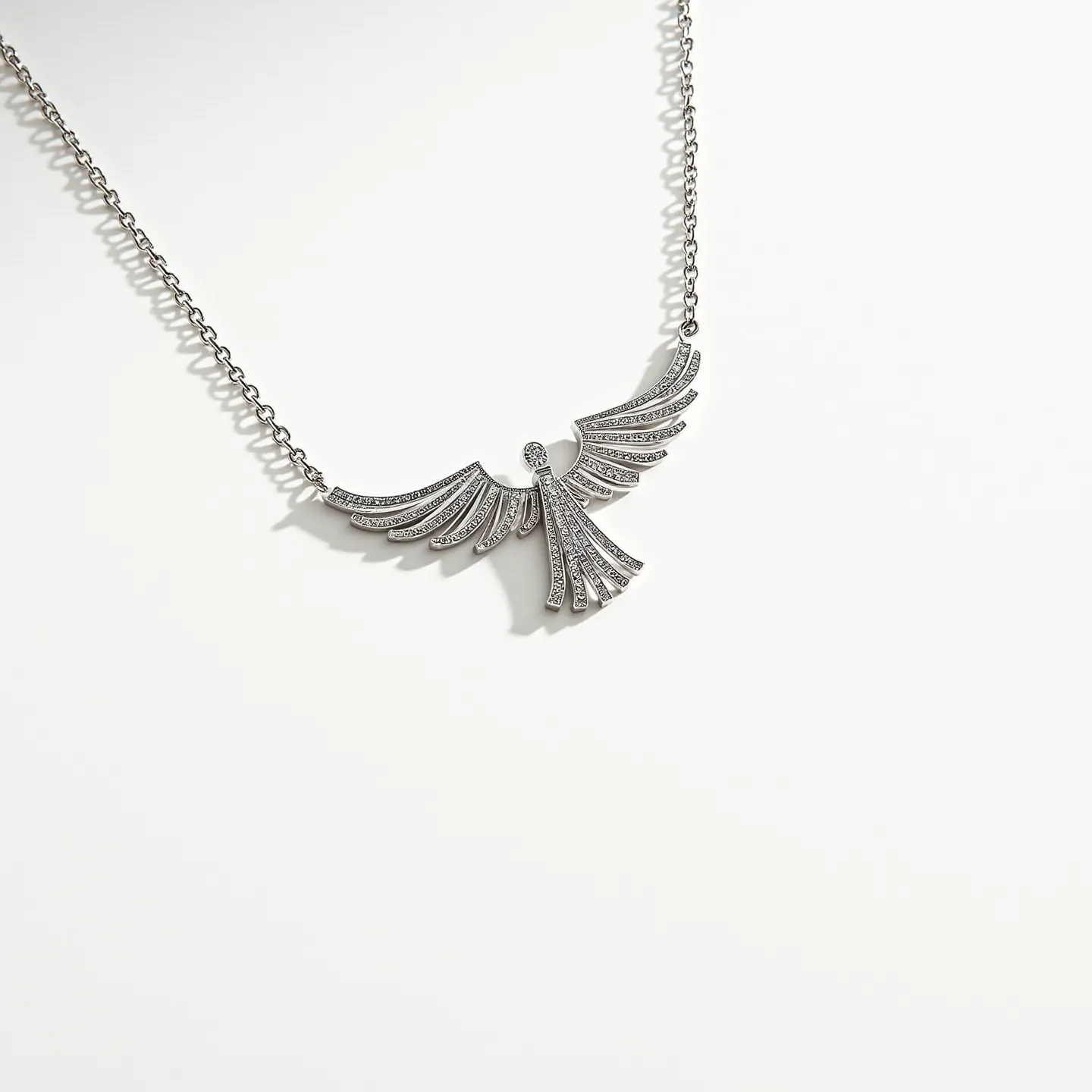 This angel necklace features a graceful, stylized angel pendant crafted from what appears to be metal, likely silver or a silver-toned alloy. The pendant is intricately adorned with small, sparkling stones, potentially diamonds or cubic zirconias, set in a pavé style that enhances the overall shimmer and elegance of the piece. The wings of the angel are prominently detailed, with the stones meticulously placed to emphasize the flowing design. The necklace is attached to a delicate chain, which may be composed of the same metal as the pendant, providing cohesion to the design. The clasp isn't visible, but it likely consists of a standard type such as a lobster clasp, ensuring both functionality and security when worn.