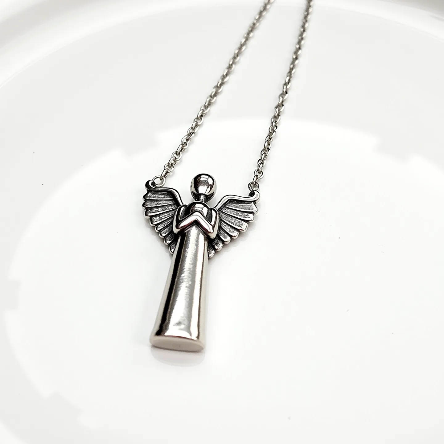 This angel necklace features a pendant shaped like an angel, crafted from what appears to be a silver-toned metal, giving it a sleek and polished finish. The design is simple yet elegant, with detailed wings extending from the figure’s back. There are no visible gemstones or intricate settings on the pendant, maintaining a minimalist appeal. The pendant is suspended on a delicate chain that matches the pendant’s metallic hue, likely secured with a standard lobster clasp for easy attachment. The overall aesthetic is serene and understated, making it a versatile piece for various occasions.