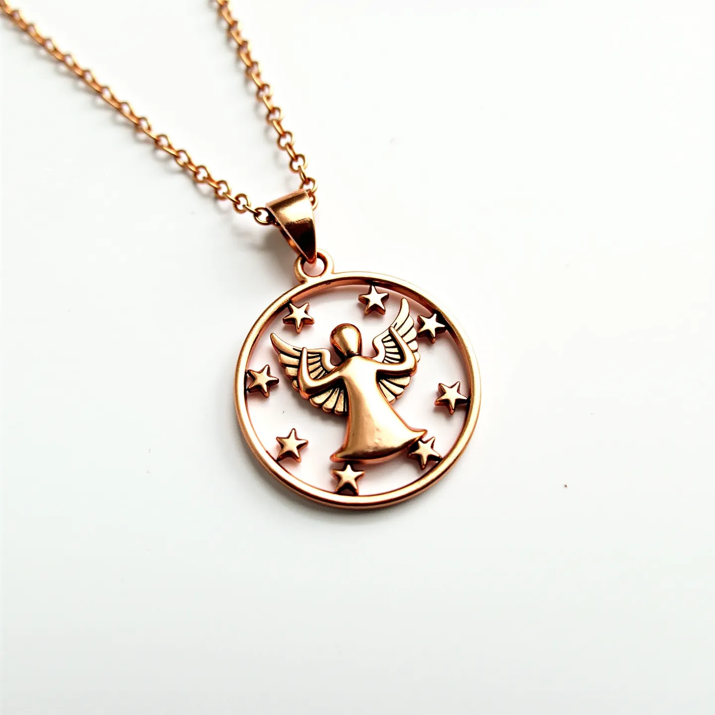 This angel necklace features a circular pendant design, crafted from what appears to be a warm rose gold-toned metal. The pendant showcases an angel figure at its center, elegantly framed by small stars, all sharing the same metallic finish for a cohesive and harmonious look. The necklace is connected via a simple loop and hangs from a delicate matching chain, which suggests durability while maintaining a refined aesthetic. The attachment to the chain is a classic jump ring, ensuring the pendant is securely held in place while also allowing for a smooth, flowing movement when worn.