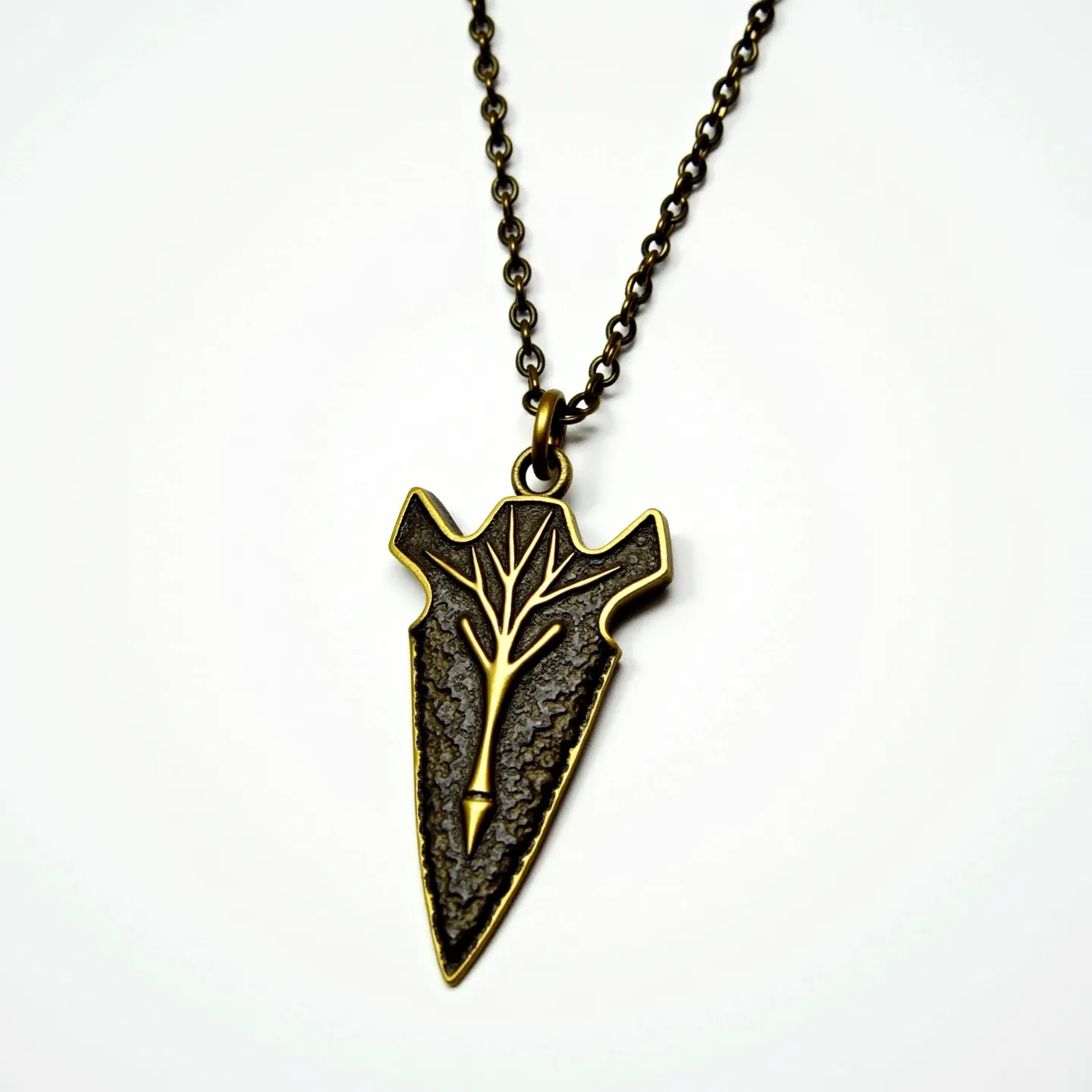 This arrowhead necklace features a pendant designed in the shape of an arrowhead, crafted from a textured metal that suggests an antique or rustic appearance. The design incorporates a prominent, stylized tree motif etched into the surface, adding a layer of visual interest and symbolism. The pendant is suspended from a metal chain with a simple circular link pattern, which complements the pendant's finish. The attachment consists of a metal loop that securely connects the pendant to the chain, ensuring stability. The chain appears to have a classic clasp mechanism, which allows for easy wear and removal.