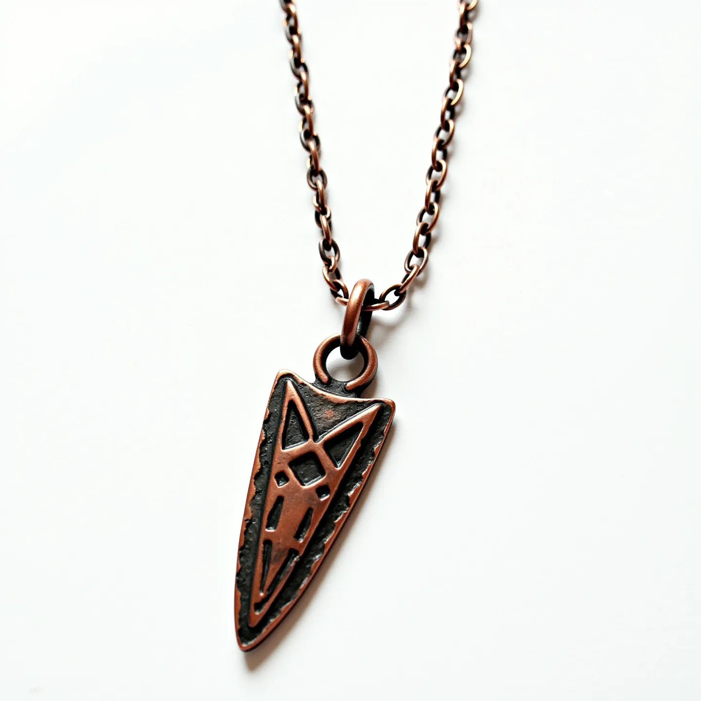 This arrowhead necklace features a distinctive pendant crafted from metal, likely with a copper or bronze finish, giving it a warm, rustic appearance. The arrowhead shape is embellished with geometric patterns, adding a touch of artistry to the piece. The pendant is suspended from a matching chain with a basic link style, and it is attached via a simple circular clasp, ensuring secure wear. The necklace does not incorporate any gemstones, focusing on the unique design of the metalwork.