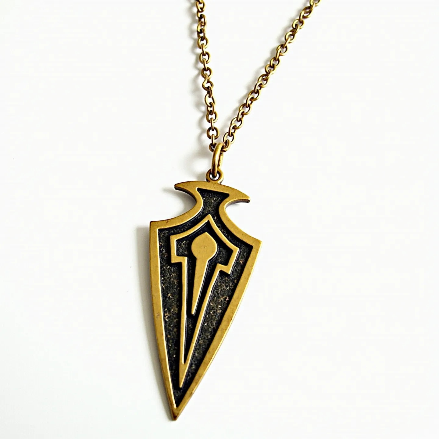 This arrowhead necklace features a pendant crafted from gold-toned metal, designed in a stylized arrowhead shape with intricate geometric patterns. The pendant lacks gemstones, focusing instead on the contrasting textures and finishes within the design. It is connected to a finely linked chain of similar gold-toned metal, enhancing the cohesive appearance of the piece. The attachment appears to be a simple loop, allowing the pendant to hang freely and adding a touch of elegance. The chain likely closes with a standard clasp, providing secure wearing while maintaining the necklace's minimalist aesthetic.