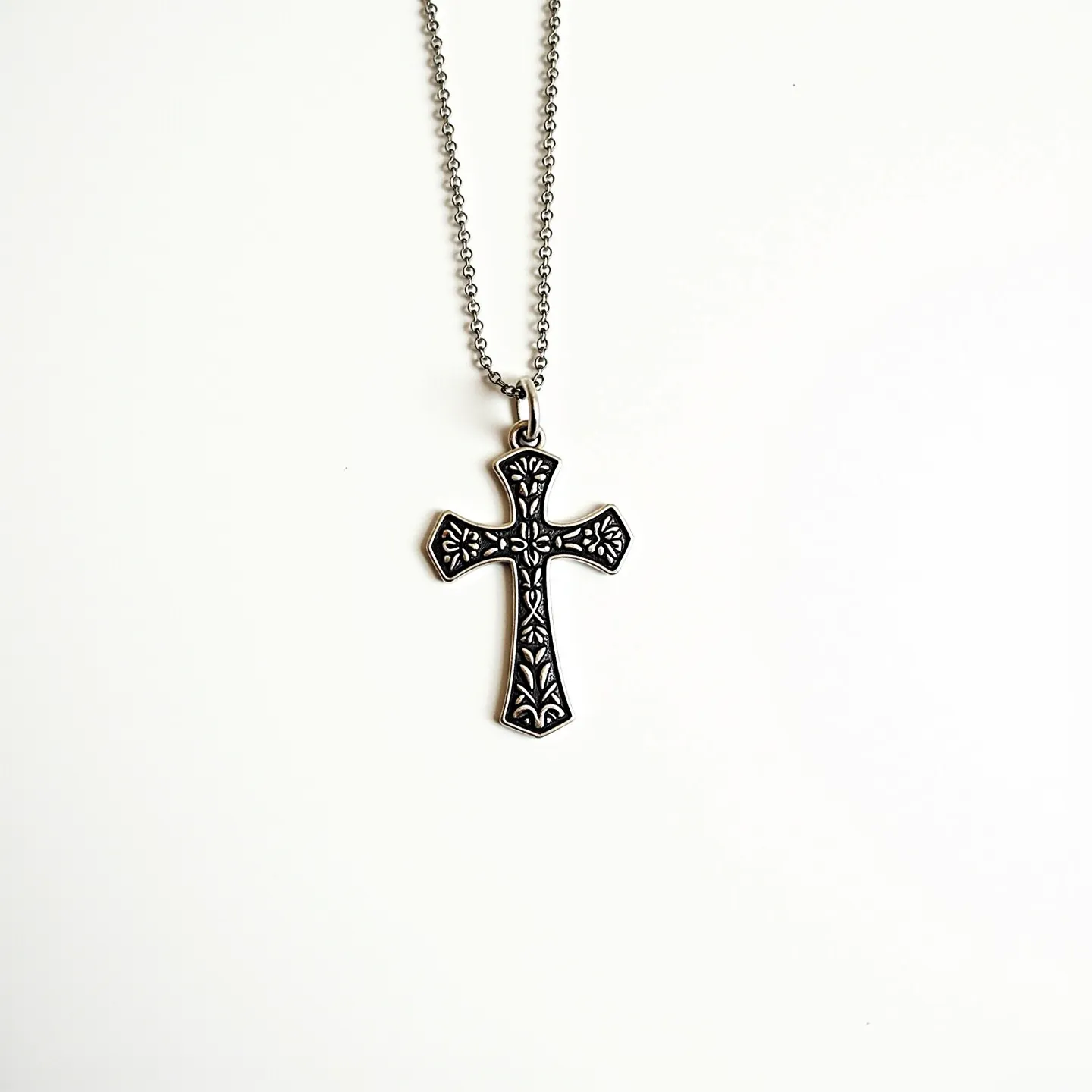 This baby cross necklace features a delicately designed cross pendant crafted from a metallic material, likely silver or stainless steel, with intricate engravings adding an ornate touch to its surface. The cross hangs from a fine chain that appears to be made of small interlocking links, providing flexibility and ease of wear. The pendant is attached to the chain with a simple, unobtrusive loop at the top of the cross, allowing it to dangle freely. The overall design is understated yet elegant, making it a suitable piece for both everyday wear and special occasions.