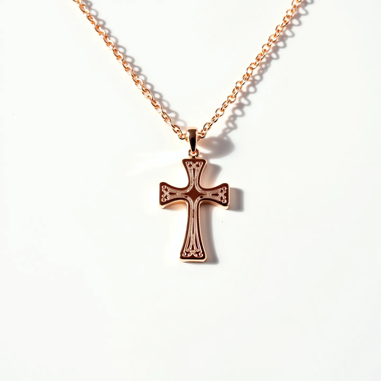 This baby cross necklace features a delicate design crafted from a warm-toned metal, possibly rose gold, with an intricate pattern etched into the front of the cross. The cross hangs from a fine chain composed of small, consistently interlinked oval links, adding subtle elegance. The pendant is attached to the chain using a small, tapered bail that secures it in place. The overall design is understated and refined, ideal for its intended delicate use.