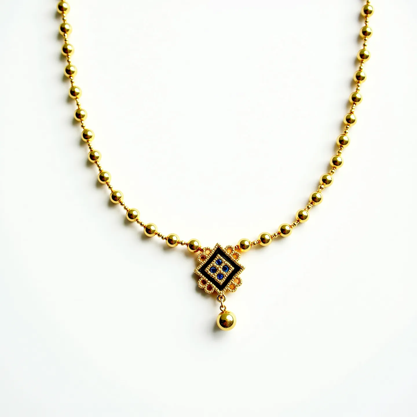 This beaded necklace features a series of uniformly sized, polished gold-colored beads strung closely together, creating a sleek and elegant chain. At the center of the necklace is a decorative pendant with a diamond-shaped design outlined in a gold frame. The pendant is adorned with small blue stones, possibly sapphires, set in a symmetrical pattern, and surrounded by intricate detailing. A single spherical drop bead hangs below the pendant, echoing the beads of the chain. The necklace likely secures with a traditional clasp at the back, maintaining its classic and refined aesthetic.