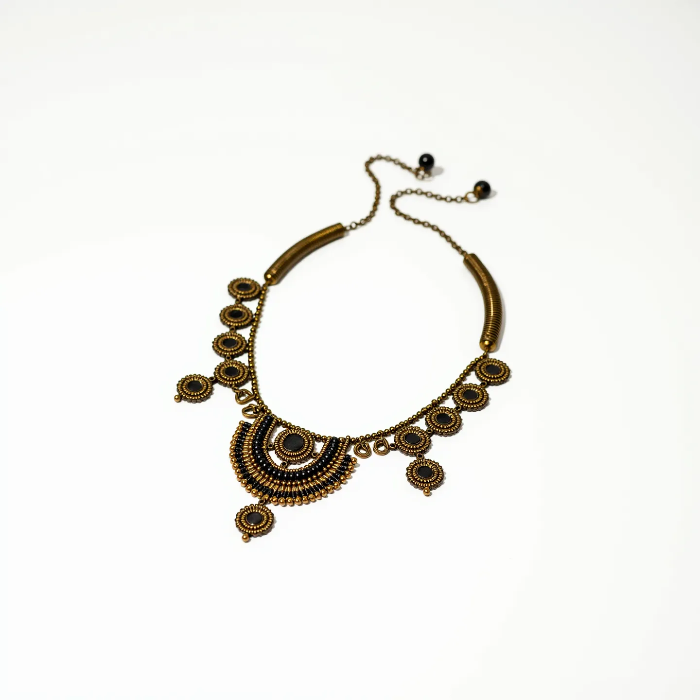 This beaded necklace features a striking design with intricate circular patterns composed of bronze-toned beads, creating a vintage and ornate look. At the center, a large, half-moon shaped pendant is adorned with concentric layers of beads, enhancing its visual appeal. The beads themselves appear to be metallic, adding a subtle shimmer to the necklace. Smaller circular bead arrangements dangle elegantly from the main chain, offering dynamic movement. The necklace is finished with a delicate bronze-toned chain, and the attachment mechanism includes a simple clasp for secure closure, allowing for easy wear.