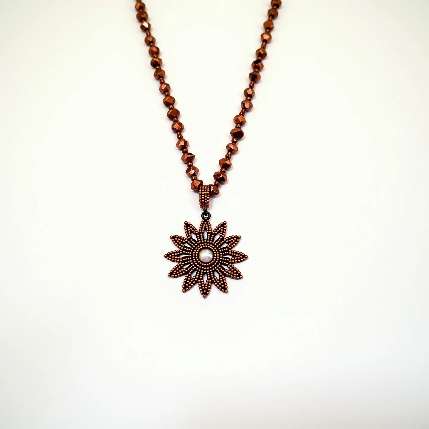 This beaded necklace features a strand of faceted brown beads, giving it an elegant and earthy look. It is accented by a striking sunflower-shaped pendant. The pendant is intricately designed with multiple petal-like elements, centered around a single round white bead, which may be a pearl or a pearl-like stone, adding a touch of sophistication to the piece. The beads and pendant are connected with detailed metallic elements that enhance the overall design.