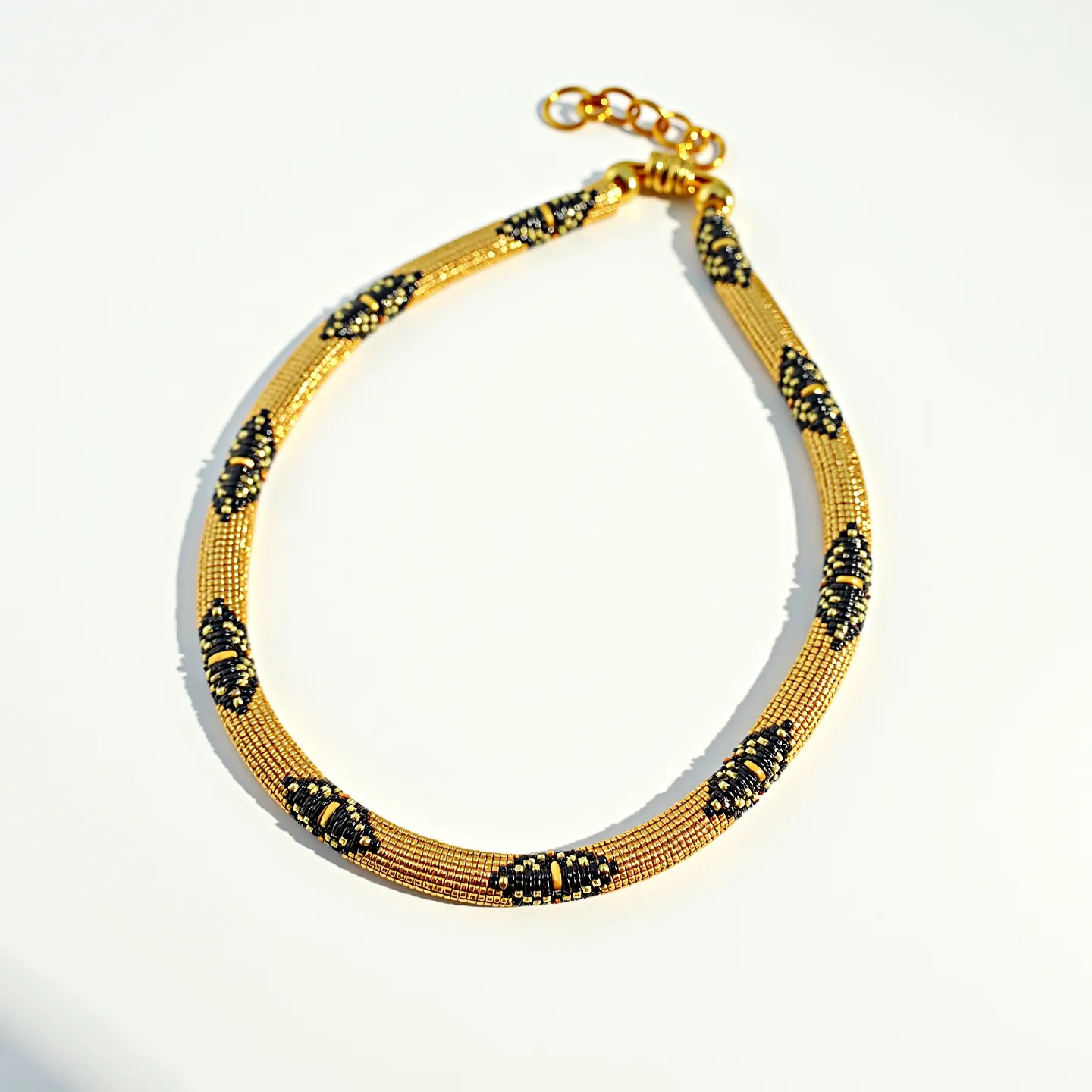 This beaded necklace is composed of meticulously arranged small, metallic beads, predominantly golden in color, creating a sleek and elegant design. Interspersed throughout the gold beads are sections of intricate black beadwork, forming symmetrical patterns that add contrast and depth to the piece. The necklace features a polished gold-tone chain extender with circular links, and it is secured by a lobster clasp, allowing for adjustable fit and ease of wear. The harmonious blend of gold and black elements in the design exudes a refined and sophisticated aesthetic.