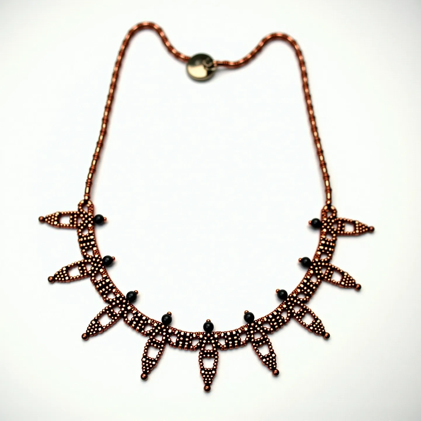 This beaded necklace features a series of intricately woven copper-colored beads forming an elegant pattern of linked arches and pointed drops. Black round beads are interspersed between the arches, adding contrast and visual interest. The necklace is finished with a circular metal clasp that complements the overall design, providing both functionality and style. The combination of colors and materials gives the necklace a vintage and handcrafted appearance, making it a striking accessory.