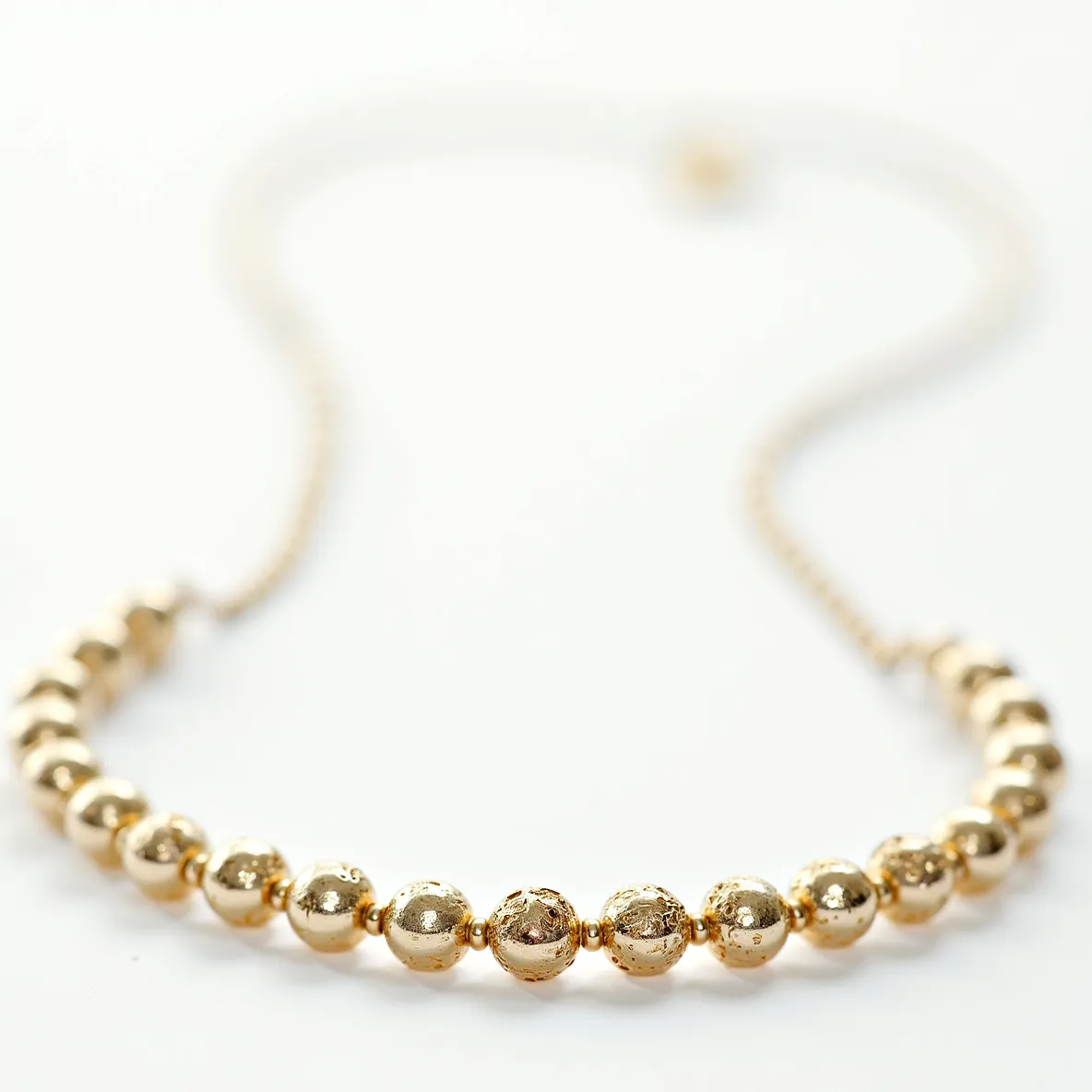 This beaded necklace features a series of spherical gold beads strung together in a classic design. The beads appear uniformly polished, displaying a lustrous and reflective surface. The necklace seems to be composed entirely of metallic elements without any visible gemstones, and the beads are likely made of gold or a gold-plated material. Each bead is evenly spaced, providing a harmonious and elegant appearance. The necklace is likely finished with a subtle clasp, possibly a lobster claw or spring ring, although the details of the attachment are not prominently visible in this image.