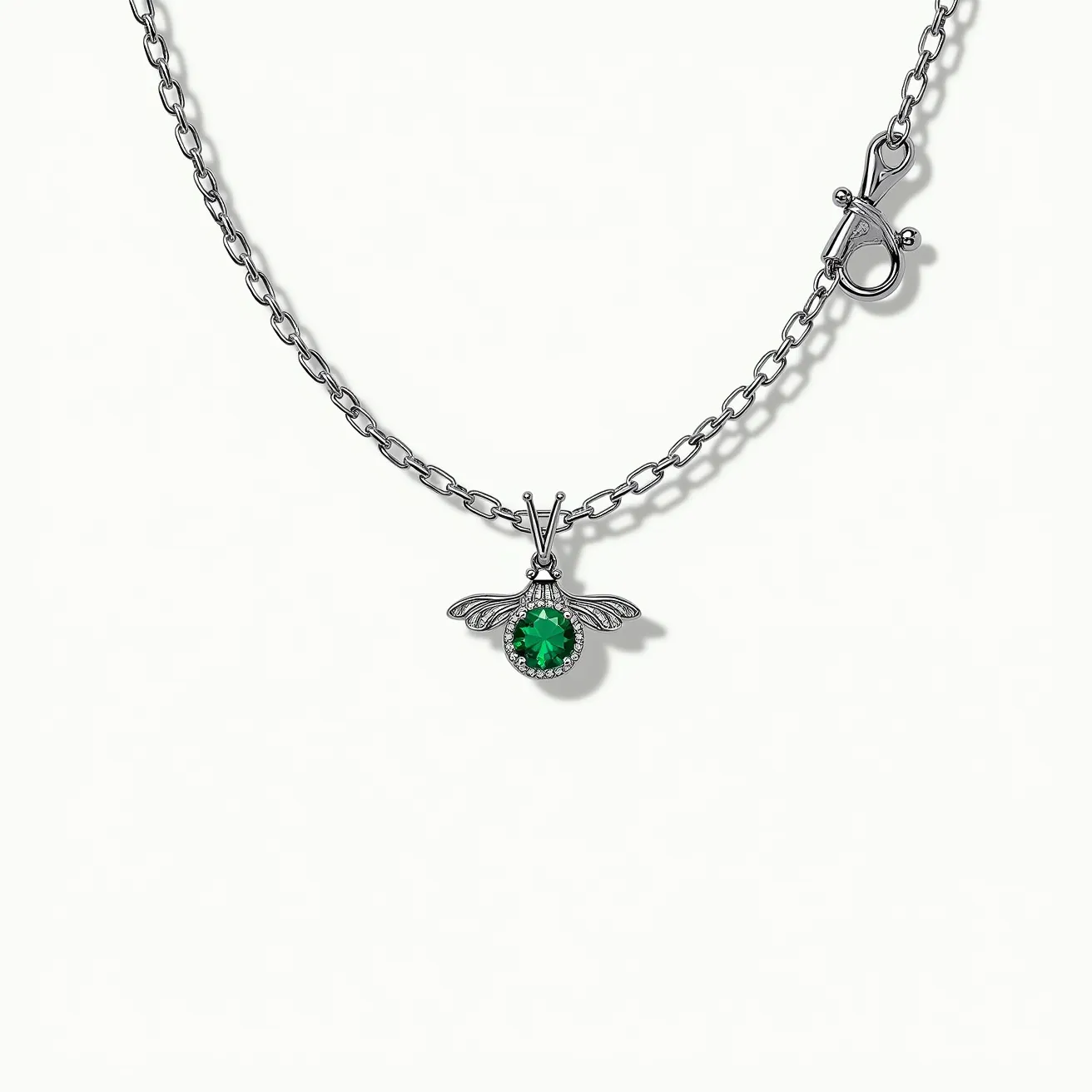 This bee necklace features a detailed bee pendant crafted from silver-toned metal, with wings extending elegantly from the body. At the center of the bee is a vibrant green gemstone, possibly an emerald or a similar stone, cut in a round shape and securely set in a bezel setting. The chain is composed of sleek, interlinked oval links, providing a sturdy yet elegant appearance. The necklace is fastened with a sophisticated lobster clasp, ensuring secure wear.