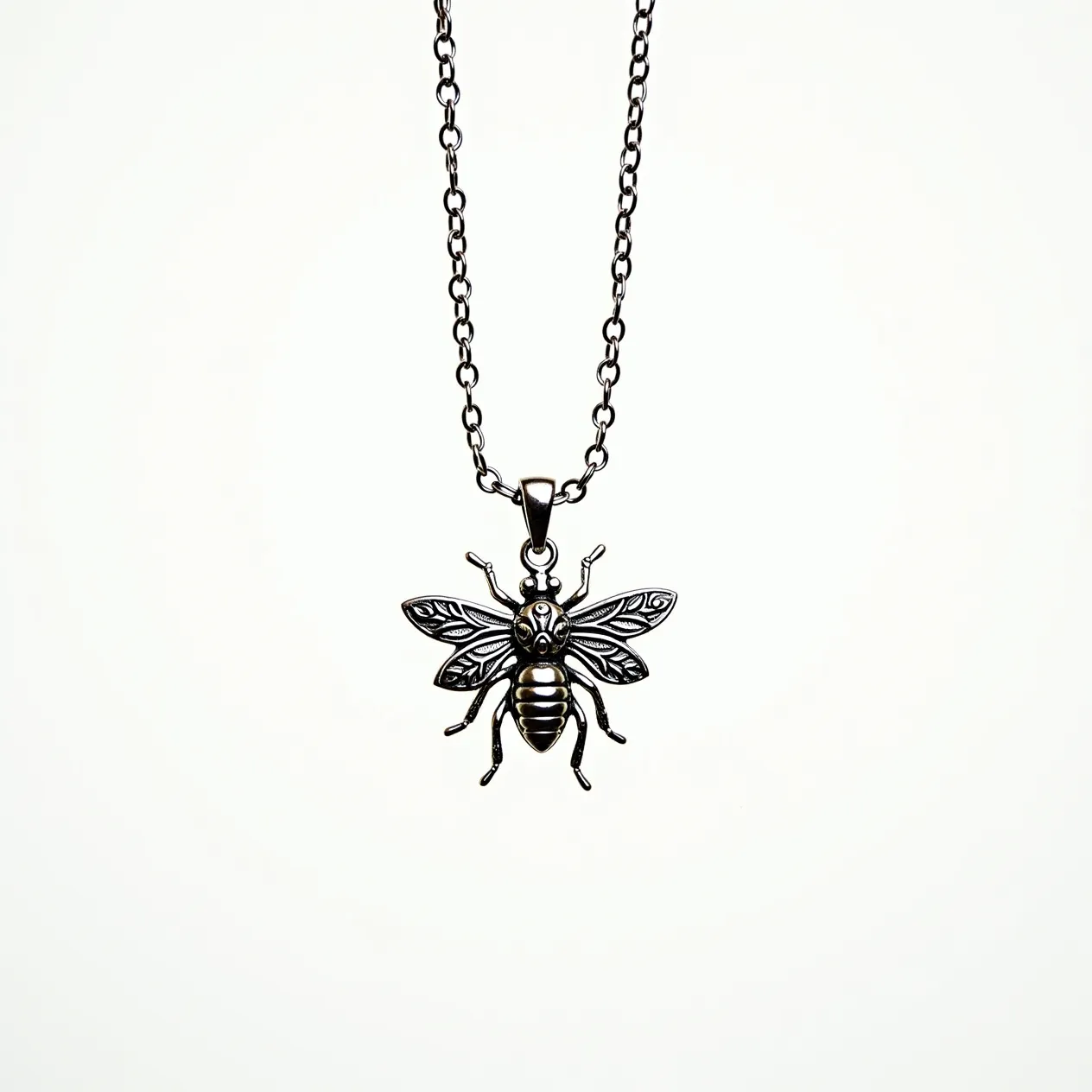 This bee necklace features a detailed pendant crafted from silver-toned metal, showcasing intricate designs on the bee's wings and body that highlight its natural elegance. The pendant hangs from a matching silver-toned chain, using a standard jump ring or bail that blends seamlessly with the necklace's overall style. The chain consists of uniform round links, secured with a lobster clasp for easy wearability. The necklace exemplifies a blend of nature-inspired artistry and classic metallic beauty, capturing attention with its delicate and refined craftsmanship.