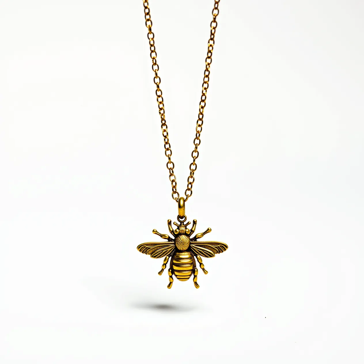 This bee necklace features a pendant intricately designed to resemble a bee, crafted from a gold-toned metal, suggesting brass or gold-plated material. The pendant displays detailed craftsmanship, highlighting the wings and body segments with precision. The necklace chain has a simple link design, also in a matching gold tone, offering consistency with the pendant. The attachment seems to be a small loop where the chain threads through, allowing the bee pendant to dangle elegantly. There are no visible gems or stones set into the piece, maintaining a focus on the metallic elements and design.