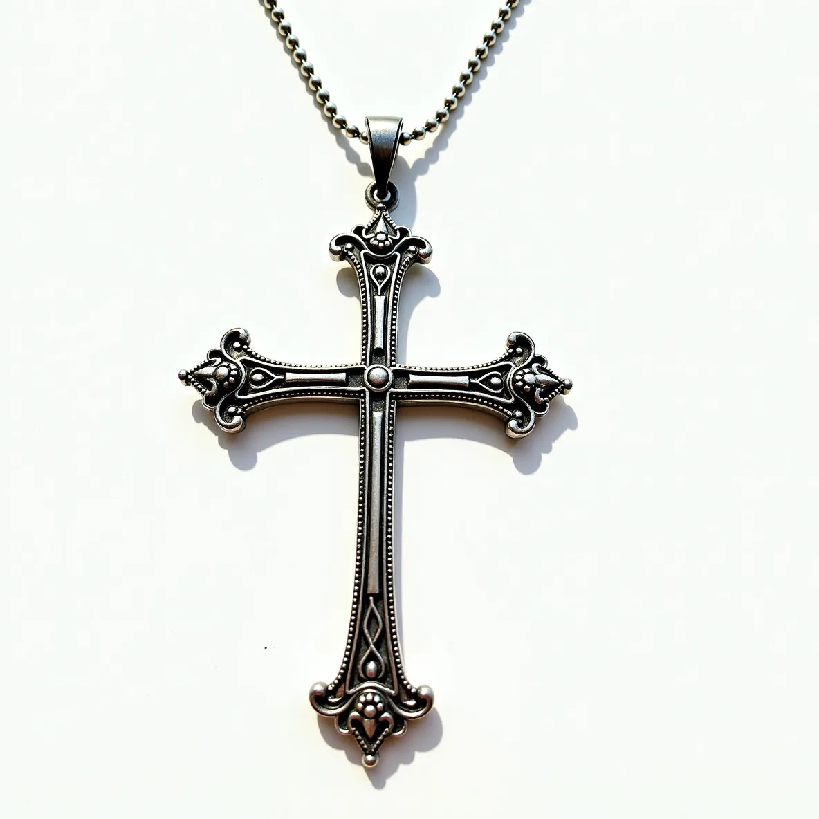 This big cross necklace features an intricate design crafted from metal with an antique silver-tone finish. The cross displays ornate detailing along each arm, with bead-like accents and swirl patterns that enhance its visual appeal. At the center of the cross, the intersection is highlighted by a raised circular mound, contributing to its decorative elements. The edges of the cross arms subtly curve, adding a touch of elegance. The pendant is attached to a metal chain through a sturdy bail, ensuring secure wear.