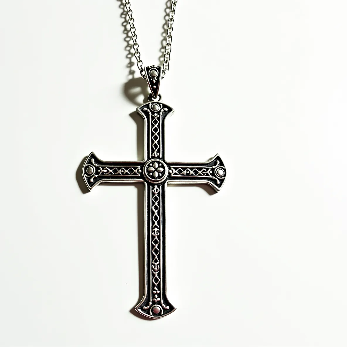 This big cross necklace features an intricate design crafted from silver-toned metal, accented with a series of small, ornate embellishments that enhance its visual appeal. The cross itself is detailed with a symmetrical pattern, which includes raised dots and lattice work that lends a texture to the piece. At the center of the cross, there is a circular motif resembling a floral design, adding to the decorative theme. The piece is equipped with a robust and sizable loop at the top, through which a sturdy chain is threaded. This chain is composed of interlinked loops, suggesting durability and a classic style, fastened with a conventional lobster clasp for secure attachment.