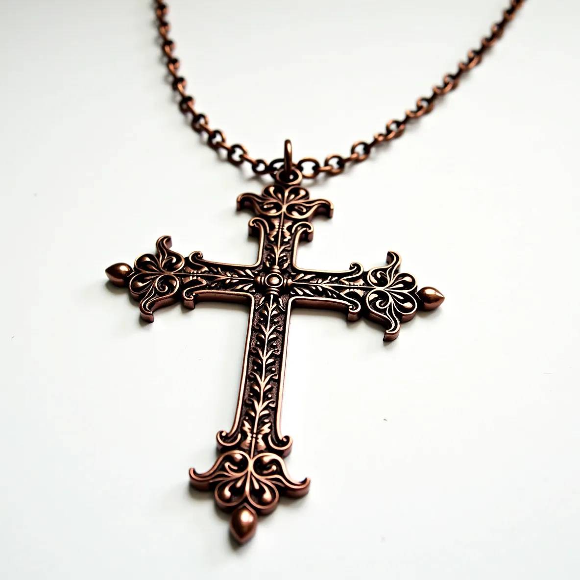 This big cross necklace features an intricate copper design with Baroque-style embellishments, emphasizing ornate and symmetrical patterns. The cross is made of polished metal with a warm, coppery finish that showcases elegant detailing along its arms. It does not appear to have any gemstones or additional settings embedded in the design. The chain, which complements the cross in color and style, includes links that connect to a sturdy loop at the top of the cross, allowing for easy attachment. The craftsmanship highlights an emphasis on vintage or antique styling, making it a bold statement piece.