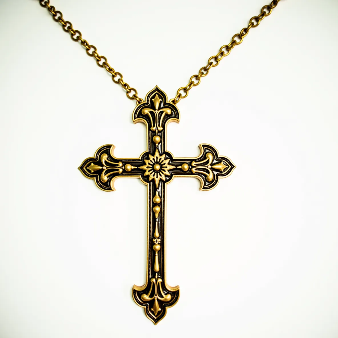 This big cross necklace features an ornate design with a combination of dark and gold-toned materials, giving it an antique appearance. The cross's intricate pattern includes floral motifs at the center and ends of the arms, highlighted by gold beading and detailing. The texture and finish suggest it might include brass or a similar metal to achieve the rich color contrast. The necklace is attached to a robust chain with links that complement the cross's decorative style, and it has a secure clasp that ensures stability and ease of wear.