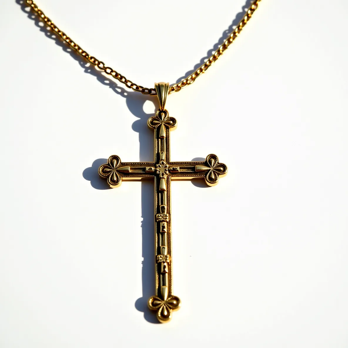 This big cross necklace features a gold-toned metal design with ornate detailing at each of the four endpoints, where a trefoil pattern is present. The central section of the cross incorporates small floral patterns, adding an intricate layer of embellishment. The cross is suspended from a chain of interlocking links, also gold-toned, contributing to a cohesive and elegant appearance. At the top of the cross, a bail attachment allows the pendant to hang securely from the chain, ensuring it remains the focal point of the necklace.