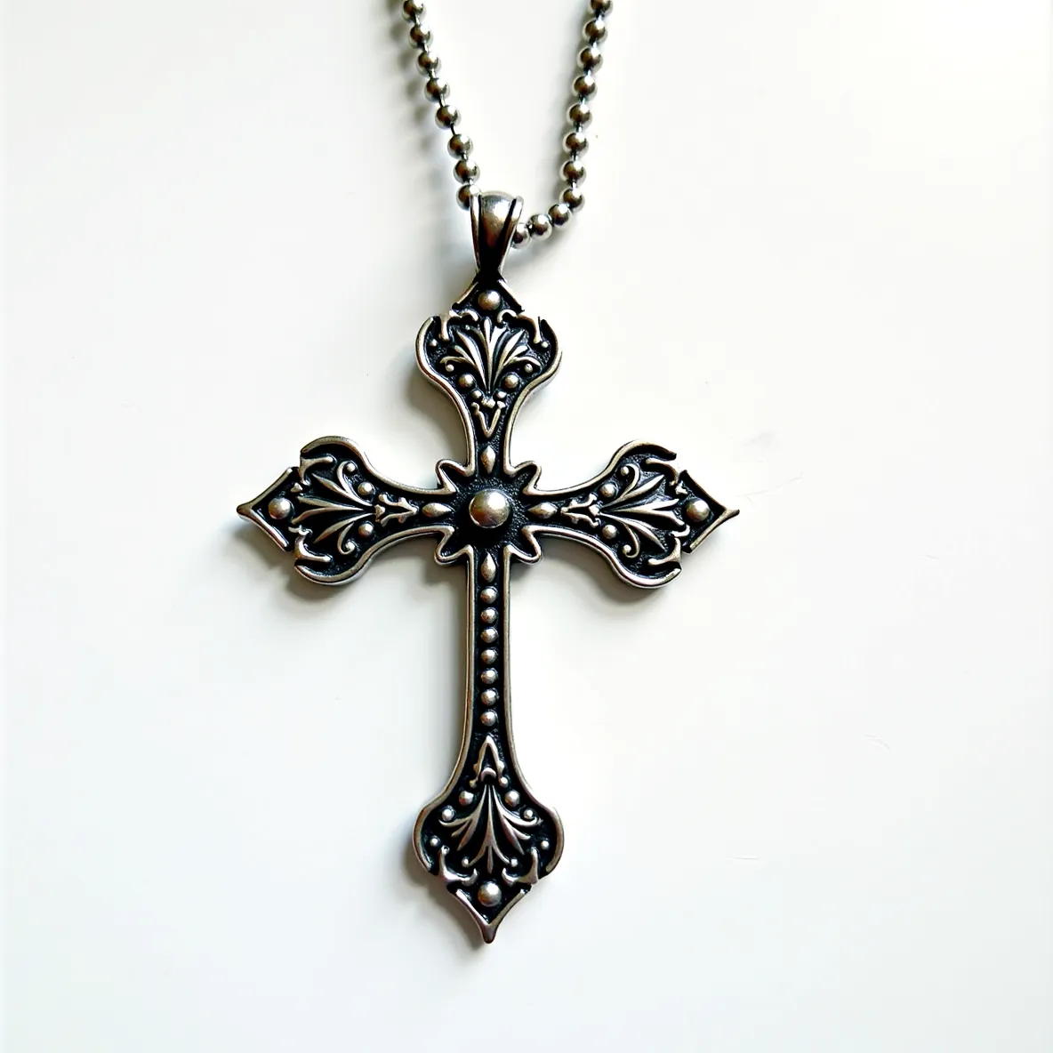 This big cross necklace features an ornate design crafted from what appears to be a silver-toned metal, adorned with intricate filigree patterns. At the center and ends of each arm of the cross are round metal accents which give an embellished look. The surface of the cross showcases a combination of smooth and raised textures, enhancing its decorative appeal. The pendant hangs from a classic bead chain, which is secured by a standard clasp typical for such designs, ensuring both functionality and style.