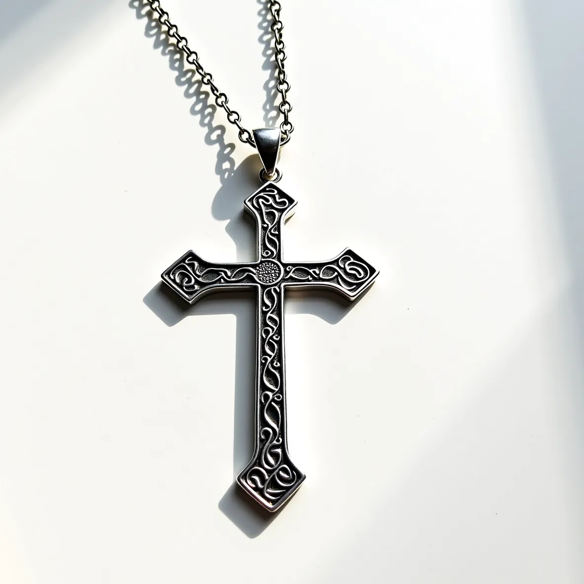 This big cross necklace features an intricately designed cross pendant made of a metallic material, possibly silver or stainless steel, showcasing ornate, swirling patterns reminiscent of Celtic or Gothic styles. The design emphasizes craftsmanship with its raised detailing and matte finish. The chain appears to be a sturdy link chain, matching the metallic tone of the pendant, and is attached to the cross via a discrete metal loop or bail. The clasp type isn't visible, but the robust nature of the chain suggests durability suitable for regular wear. The design is elegant, with a unisex appeal, devoid of any gems or stones, which enhances its classic and versatile appearance.