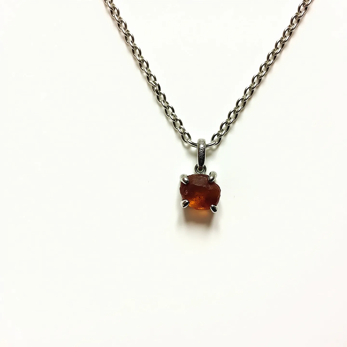 This birthstone necklace features a sterling silver chain with a natural, uncut garnet as the centerpiece. The chain is a simple cable design, providing a sturdy and elegant base for the pendant. The garnet is set in a four-prong setting, allowing the stone's rich red color to be the main focal point. The pendant is attached to the chain with a small bale, seamlessly integrating with the overall design. The necklace is completed with a standard clasp, ensuring it stays securely in place when worn.