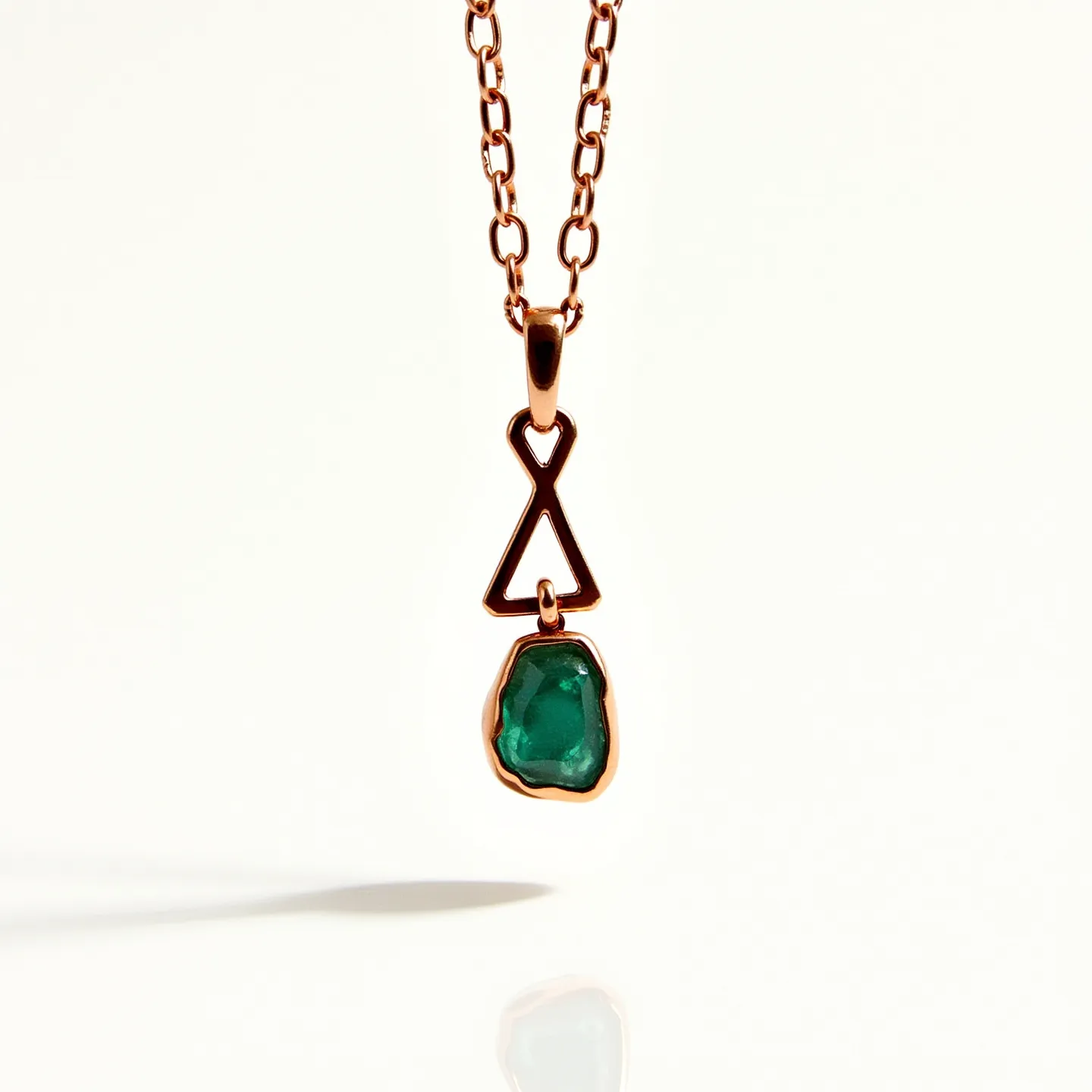 This birthstone necklace features a striking green gemstone, likely an emerald, which is irregularly cut to showcase its natural beauty. The stone is set in a polished metal frame that appears to be rose gold, adding an elegant contrast to the vibrant green gem. The pendant hangs from a chain with links that match the rose gold setting, enhancing the overall harmony of the design. The necklace is equipped with a unique clasp, using a geometric triangle and loop design, which complements the artistic style of the pendant.