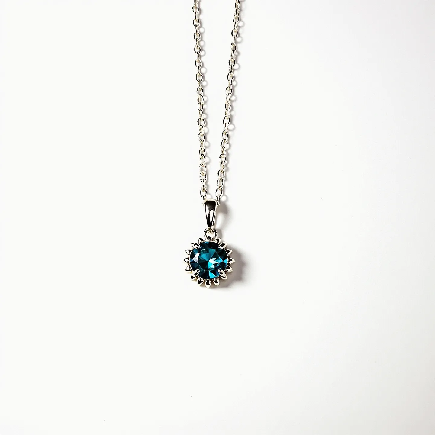 This birthstone necklace features a striking blue gemstone, likely a round-cut birthstone, set in a detailed, sunflower-inspired bezel setting. The pendant is elegantly attached to a delicate silver chain, which highlights the brilliance of the stone. The chain is connected with a classic lobster clasp, ensuring both security and ease of use. The silver finish complements the vibrant hue of the gemstone, making the necklace a versatile piece for different outfits and occasions.