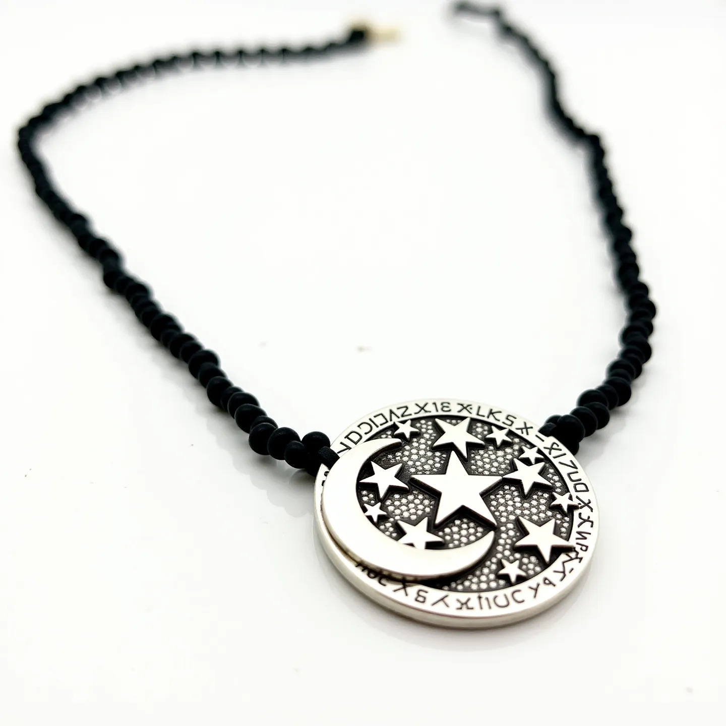 This black choker features a strand of small black beads, crafted from what appears to be either glass or polished stone, providing a sleek, uniform look. The centerpiece is a round metal pendant with intricate cut-out designs of stars and a crescent moon, encircled by a series of symbols or letters, likely of a decorative or symbolic nature. The pendant is set with a detailed background that enhances the celestial motif, giving depth and texture to the design. At the back, the choker is completed with a simple metal clasp, ensuring a secure and adjustable fit around the neck. The overall style combines a touch of mysticism with classic elegance.