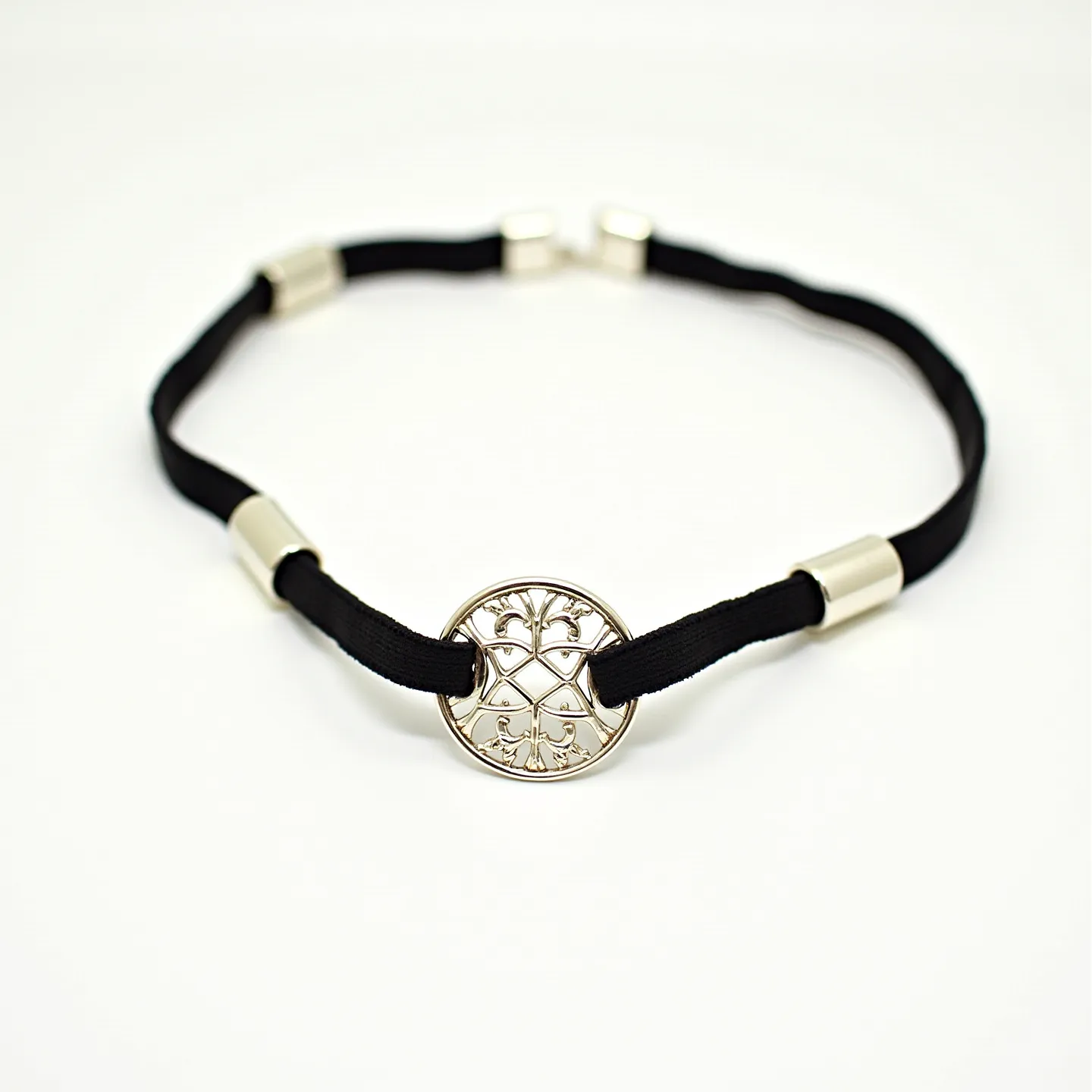 This black choker features a sleek black band, likely made of a soft fabric or velvet material, providing a smooth and comfortable fit around the neck. The choker is characterized by a central round metallic charm, intricately detailed with a decorative design, adding an elegant focal point. The charm appears to be crafted from a polished metal, possibly silver or stainless steel, reflecting light and enhancing its visibility. Along the band, there are smooth, cylindrical metallic accents that complement the central charm and add to the overall aesthetic. The choker also includes a metal clasp at the back, offering a secure and adjustable closure, ensuring ease of wear and removal.