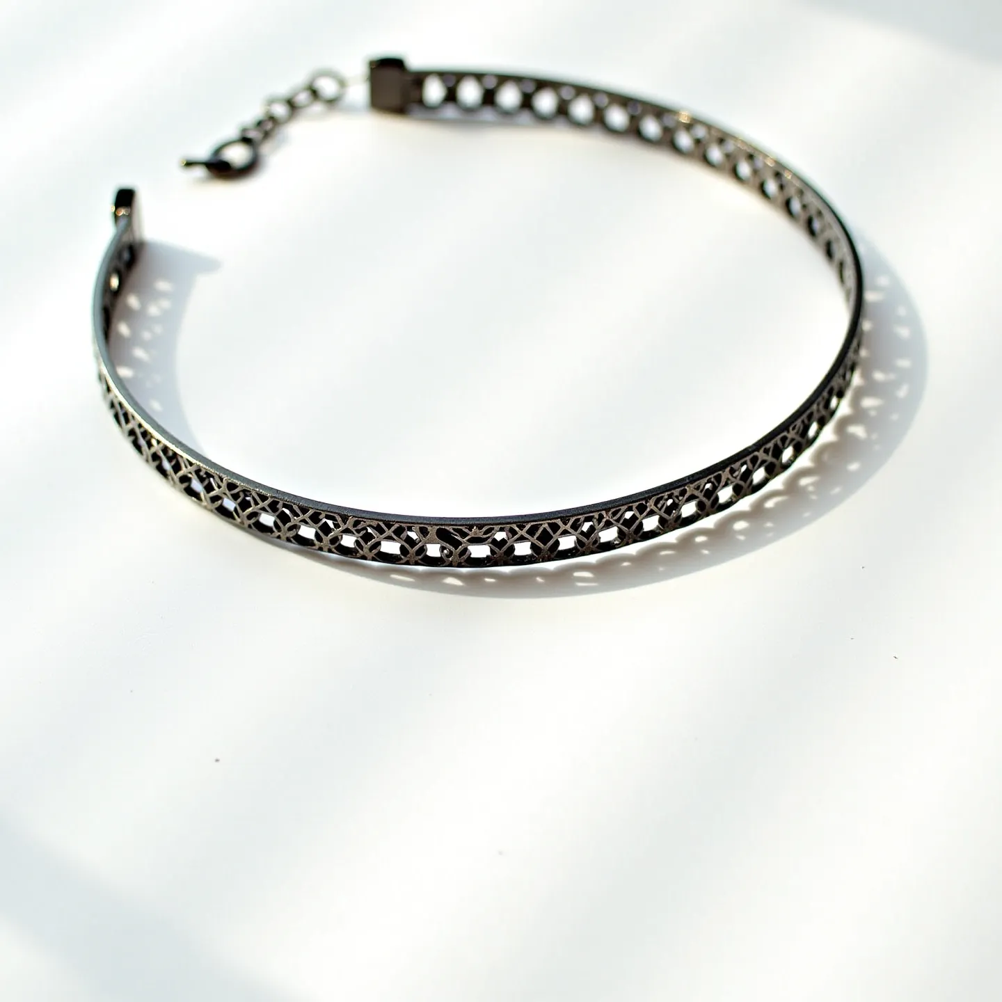 This black choker features an intricate lattice design crafted from a metal material that gives it a sturdy yet elegant appearance. The pattern showcases a series of interwoven loops that create a visually appealing texture, adding depth to its design. It is equipped with a lobster clasp and an adjustable chain, allowing for a customizable fit. The choker’s sleek and polished finish provides a subtle shine, while the absence of gemstones keeps its overall look minimalist and versatile.