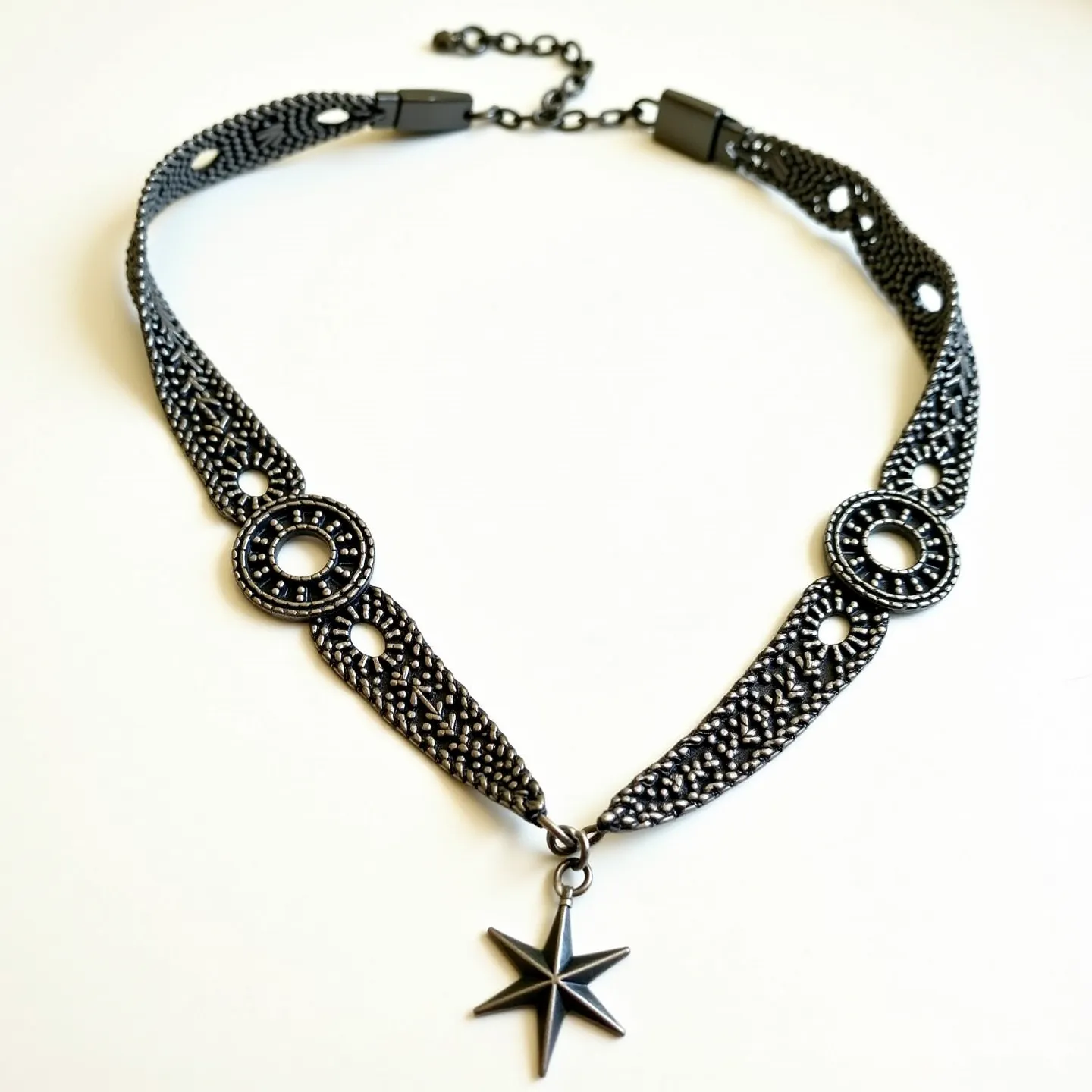 This black choker features intricately designed black metalwork, likely made from oxidized silver or a similar dark alloy, creating a vintage and elegant appearance. The choker includes round circular motifs evenly spaced along the band, offering a sophisticated pattern enhanced with delicate bead-like detailing. A distinct six-pointed star pendant hangs at the center, adding a focal point with a touch of celestial charm. The choker is secured with a chain and clasp mechanism at the back, which includes an adjustable extension for versatile sizing, making it both stylish and functional.