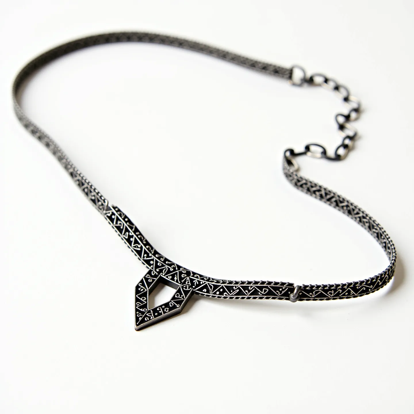 This black choker features an intricate design with a geometric centerpiece accentuated by a pattern reminiscent of tribal or ancient motifs. The choker appears to be made of a metal material with a dark finish, possibly oxidized silver, giving it a textured and ornate look. The pattern on the choker likely involves etched or engraved details, creating a contrast that highlights its delicate craftsmanship. It is equipped with an adjustable clasp, allowing for flexibility in fit, and an additional chain link for secure fastening around the neck.