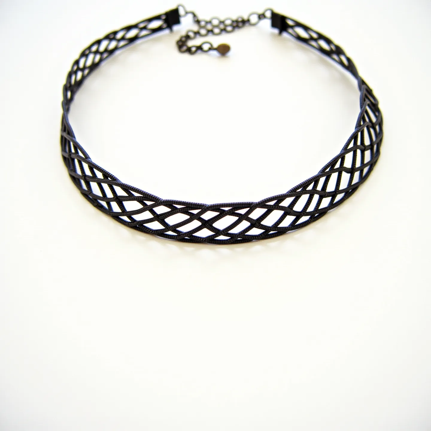 This black choker features a lattice design crafted from a sturdy metal or synthetic material, creating an intricate pattern that encircles the neck elegantly. The piece is designed with an adjustable chain at the back, allowing for a customizable fit, and is secured with a lobster clasp. The absence of gems or stones emphasizes the boldness of the geometric pattern, making it a versatile accessory that can enhance a variety of outfits.