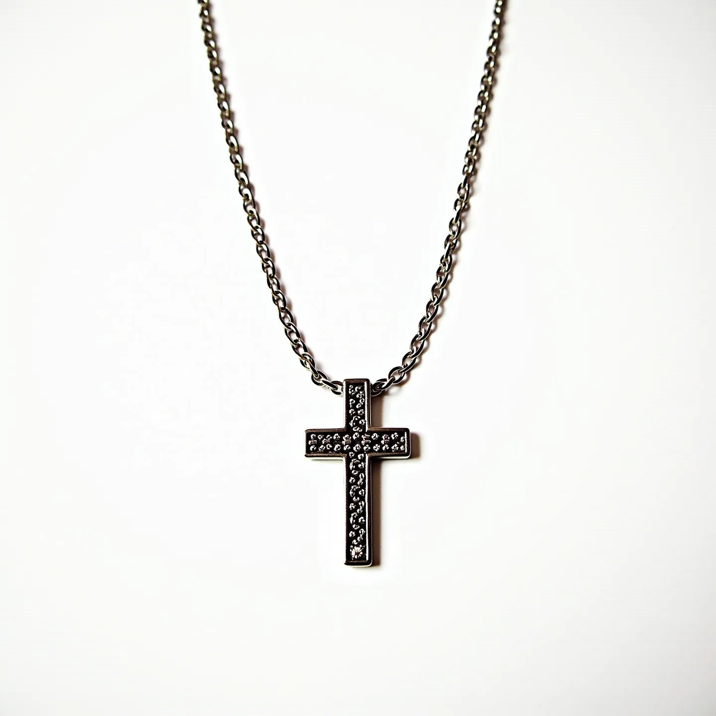 This boy's cross necklace features a cross pendant adorned with small, round, clear stones set into its surface, likely mimicking diamonds or a similar gemstone. The stones are uniformly distributed across the front of the cross, adding a sparkling element to the design. The cross itself appears to be made from a polished metal, possibly stainless steel or a similar alloy, providing a sleek and modern aesthetic. The necklace chain is a classic cable link design, which complements the pendant's style and is likely made of the same metal as the pendant for a cohesive look. The necklace is fastened with a standard lobster clasp, offering a secure and adjustable fit.