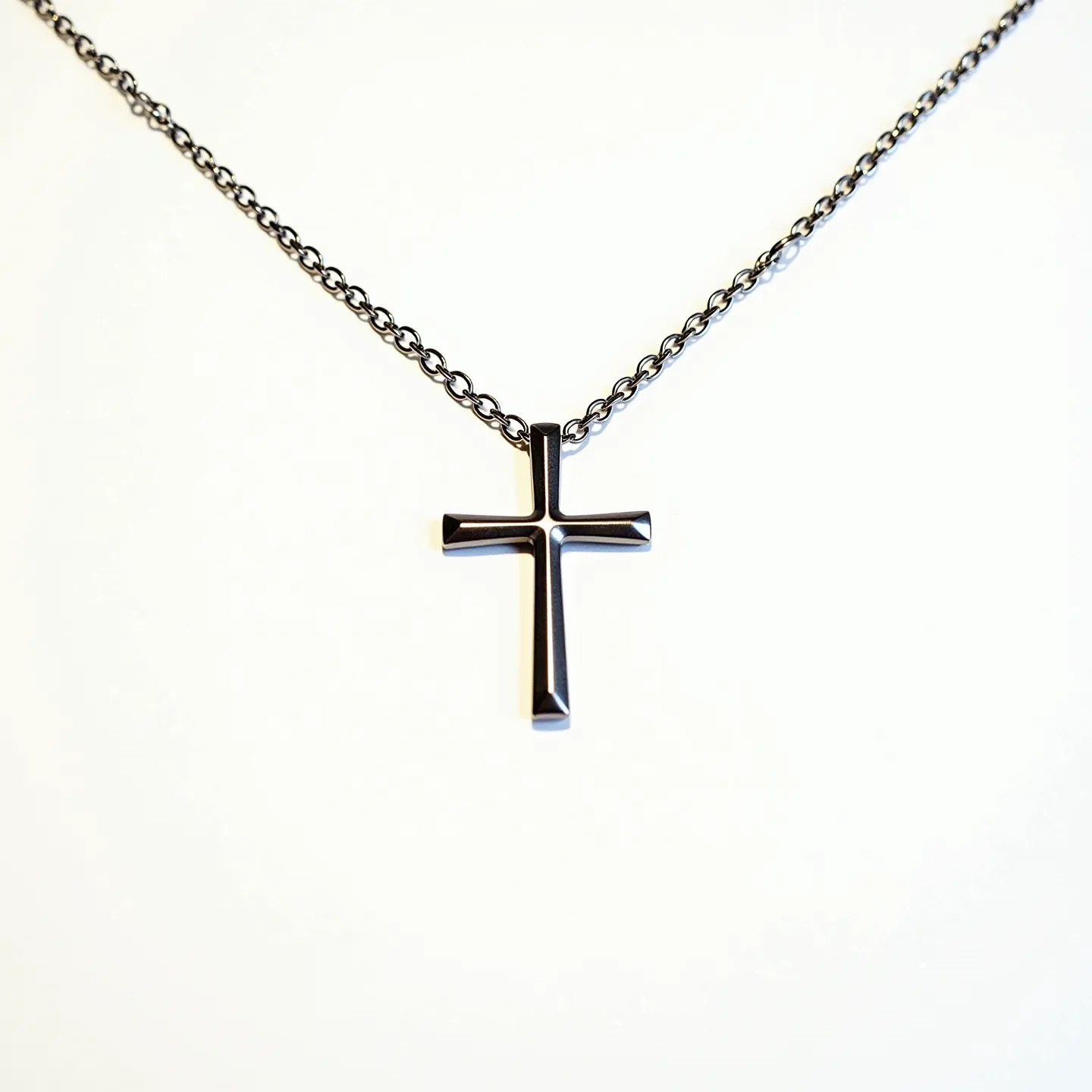 This boys' cross necklace features a sleek and minimalist design, with the cross pendant likely crafted from a metallic material with a reflective black finish, lending a modern and understated elegance. The cross is suspended from a chain that appears to be of medium gauge and made from a similar or complementary metal, providing a cohesive look. There are no visible gems or stones embedded in the pendant, which maintains a smooth, uniform surface with rounded edges. The attachment of the cross to the chain is a simple, integral component that matches the overall sleek design, ensuring durability while maintaining a seamless appearance.