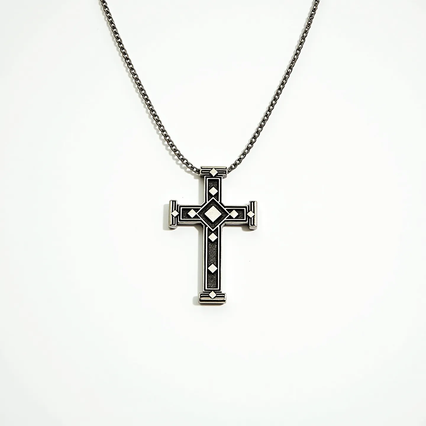 This boys cross necklace features a striking design with a silver or metal cross pendant adorned with geometric patterns. The central motif includes diamond-shaped elements suggestive of inlaid stones, which could potentially be crafted to resemble gems, neatly integrated into the design. The cross has a robust and detailed construction, displaying a border that emphasizes its intricate style. The pendant is attached to a slender chain, commonly made from a matching metal that complements the cross. The necklace likely includes a clasp for secure wear, ensuring practicality along with its visual appeal.