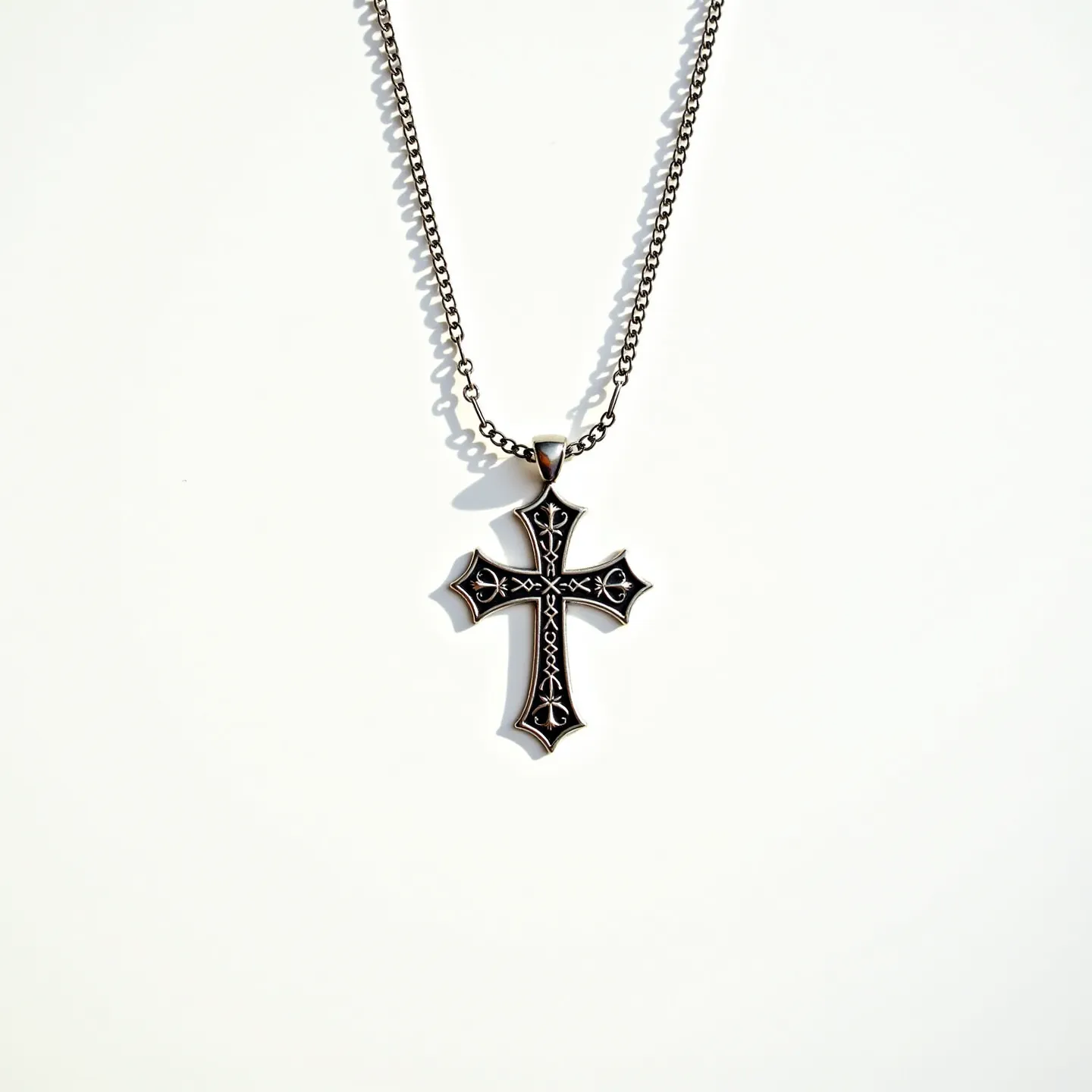 This boys cross necklace features a detailed design with intricate carvings that give it a distinct appearance. The cross is made of a polished metal that exhibits a smooth, reflective surface, likely stainless steel or a similar alloy. The pendant boasts delicate engravings without any inset gems or stones, focusing on the craftsmanship of the metal itself. The chain is a standard link style, providing a sturdy attachment, and is connected to the cross through a simple metal loop attachment, ensuring durability and wearability.