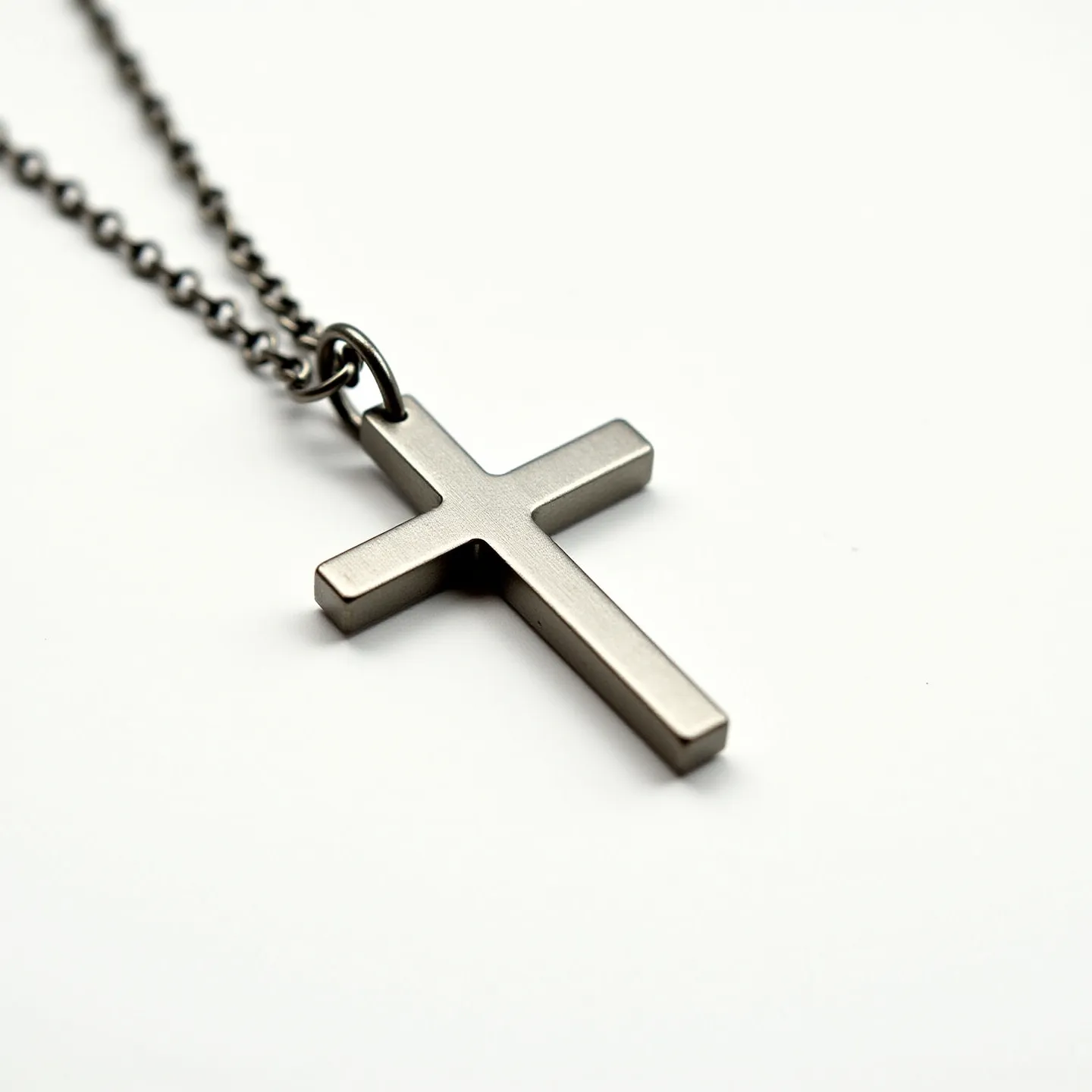 This boy's cross necklace features a sleek, metallic pendant in a classic cross shape, likely crafted from stainless steel, giving it a modern and understated appearance. The pendant has a smooth, polished surface without any embellishments such as gems or stones, highlighting its minimalist design. It hangs from a durable chain, also metallic, which ensures sturdiness and complements the pendant's finish. The cross is attached to the chain via a small circular loop, allowing for slight movement and flexibility. The necklace likely features a simple clasp to secure it around the neck, though the specific style of clasp isn't visible in the provided image.