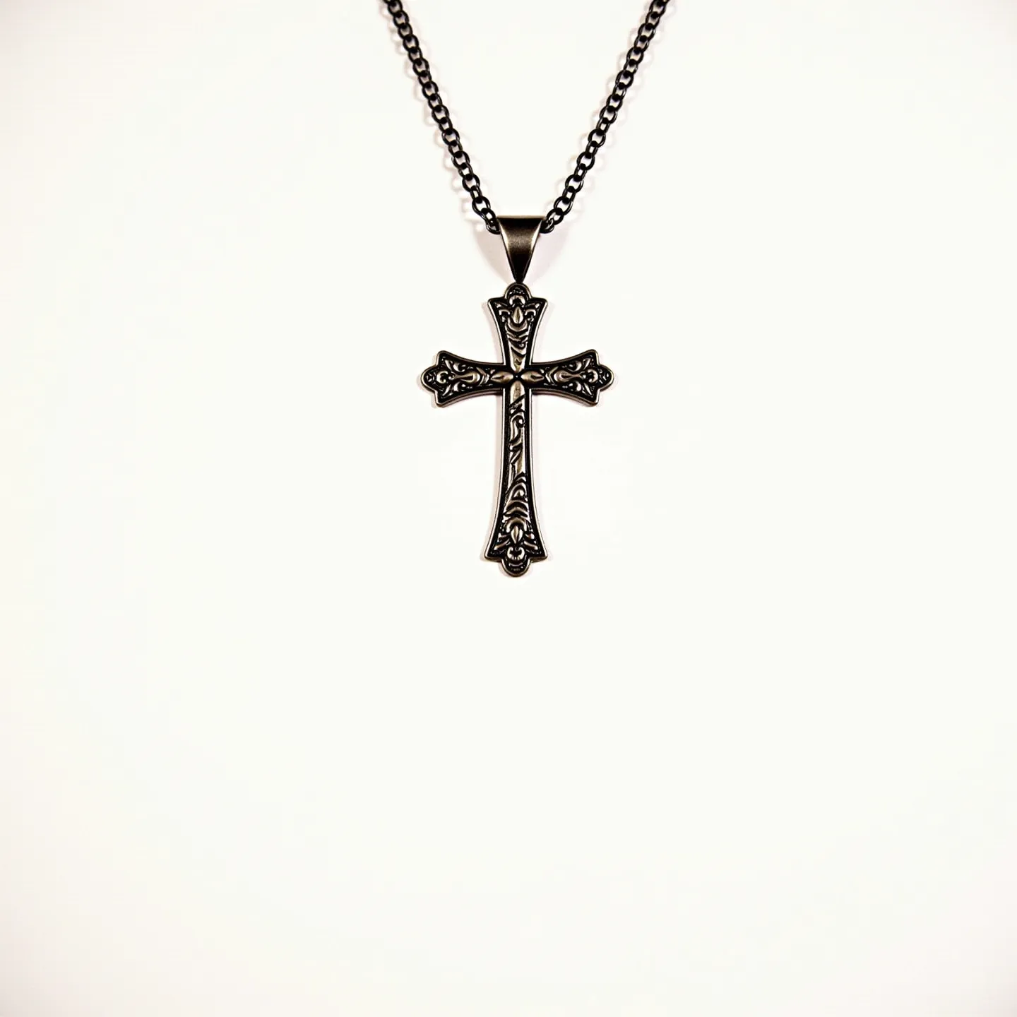 This boy's cross necklace features an intricately designed metallic cross pendant, likely made of stainless steel or a similar material, known for its durability and shine. The surface of the cross is adorned with ornate patterns, providing a gothic or vintage aesthetic. The pendant is attached to a fine chain with a similar dark metallic finish, enhancing its overall cohesive look. The design is free from any gemstones or embellishments, emphasizing the craftsmanship of the metalwork. The necklace is completed with a typical lobster clasp, ensuring secure and easy fastening.