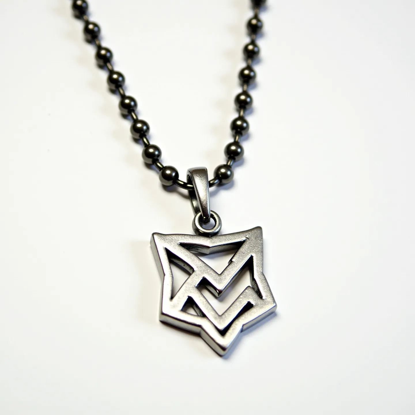 This boy's necklace features a stainless steel chain composed of small, spherical beads linked together, offering a robust and modern appearance. The pendant, also made of stainless steel, is an intricately designed geometric shape, perhaps inspired by a minimalist or abstract style, featuring sharp angles and intersecting lines. The pendant is attached to the chain with a sleek metal loop, providing a secure connection and smooth articulation. The metallic finish of both the chain and the pendant ensures durability and a contemporary aesthetic. The necklace likely utilizes a simple ball chain clasp, which is cohesive with the overall design, ensuring ease of use and reliability.