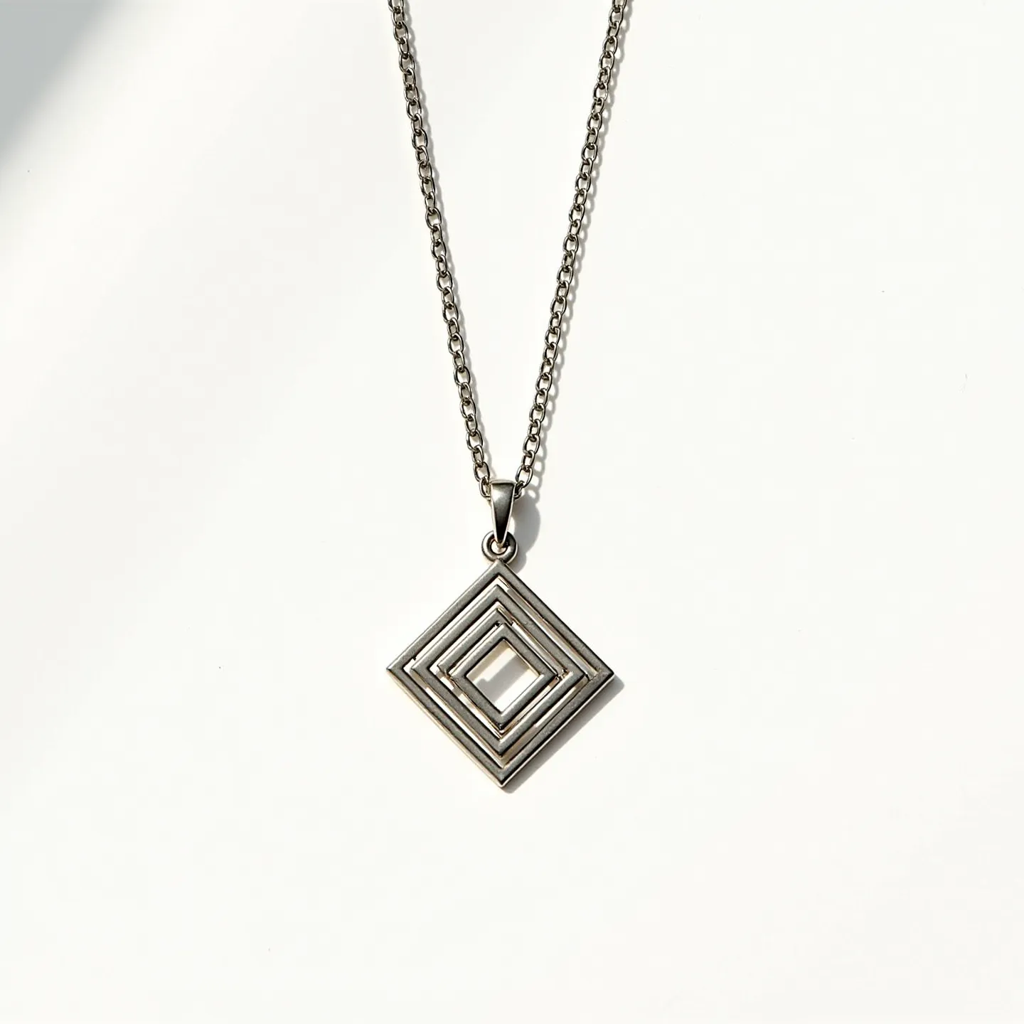 This boy's necklace features a simple, elegant design with a silver-toned chain, suggesting it may be made from stainless steel or another metal with a similar finish. The pendant is a geometric square shape with layered, concentric square patterns, giving it a modern, minimalist appeal. There are no visible gems or stones on the pendant, which is suspended from a small metal loop that seamlessly connects to the chain. The chain appears to terminate with a standard clasp for easy attachment, maintaining the necklace's cohesive and sleek aesthetic.