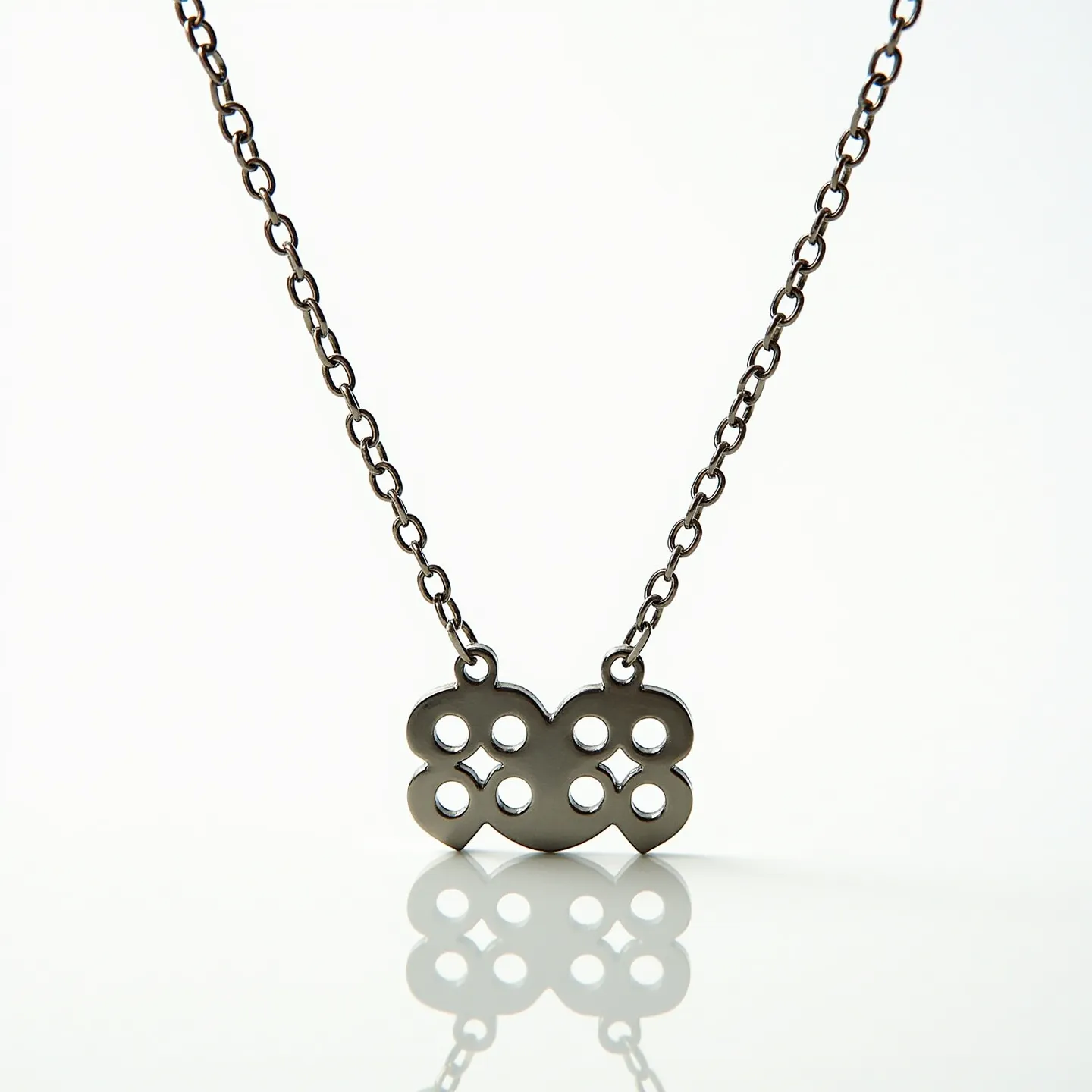 This boy's necklace features a pendant crafted from a dark metal material, designed in an intricate pattern resembling interlinked loops or floral motifs. The pattern contains multiple circular cut-outs that enhance its visual appeal. The pendant is suspended from a dark metal chain with uniformly sized, oval links providing a simple yet stylish look. The necklace likely uses a standard clasp, typical for such jewelry, to ensure secure attachment. There are no gems or stones integrated into the design, emphasizing the pendant's artistic metalwork.