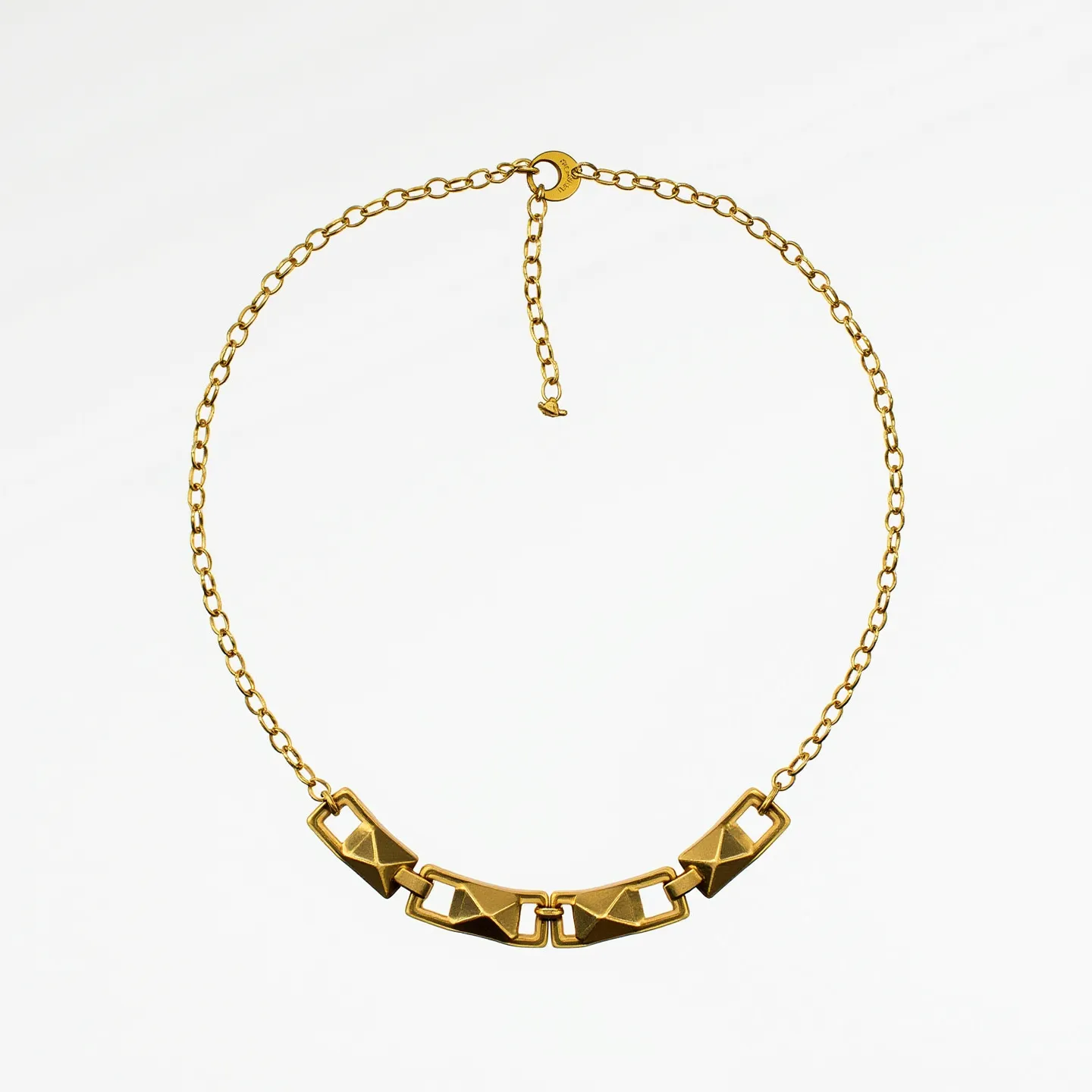 This boy's necklace features a gold-toned metal chain with a series of linked geometric pieces at the center. The main section consists of angular links, each with a pyramid-like raised surface, giving the necklace a textured and modern appearance. The necklace appears to have an adjustable length, thanks to the extended chain and a circular clasp that facilitates easy fastening. The chain links are oval-shaped and connect seamlessly with the centerpiece, creating a cohesive design. There are no visible gems or stones on this necklace, focusing instead on the metalwork for its aesthetic appeal.