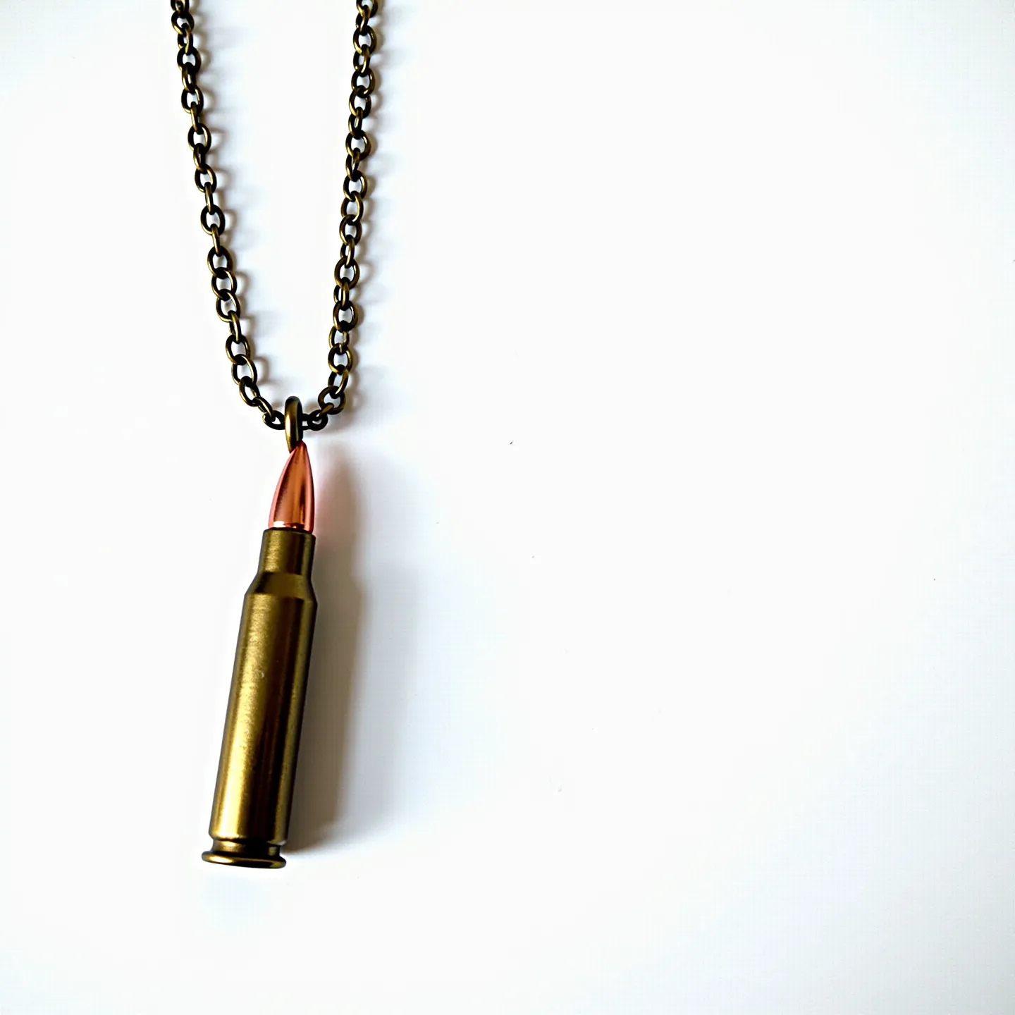 This bullet necklace features a pendant made from a brass-colored bullet casing with a copper-colored tip, giving it an industrial and rugged appearance. The bullet is attached to a sturdy, metal chain with a dark finish, adding to its bold style. The chain is linked through a metal loop at the top of the bullet, providing a secure attachment. The overall design combines metallic hues to create a striking piece of jewelry that balances raw aesthetics with a touch of sophistication.