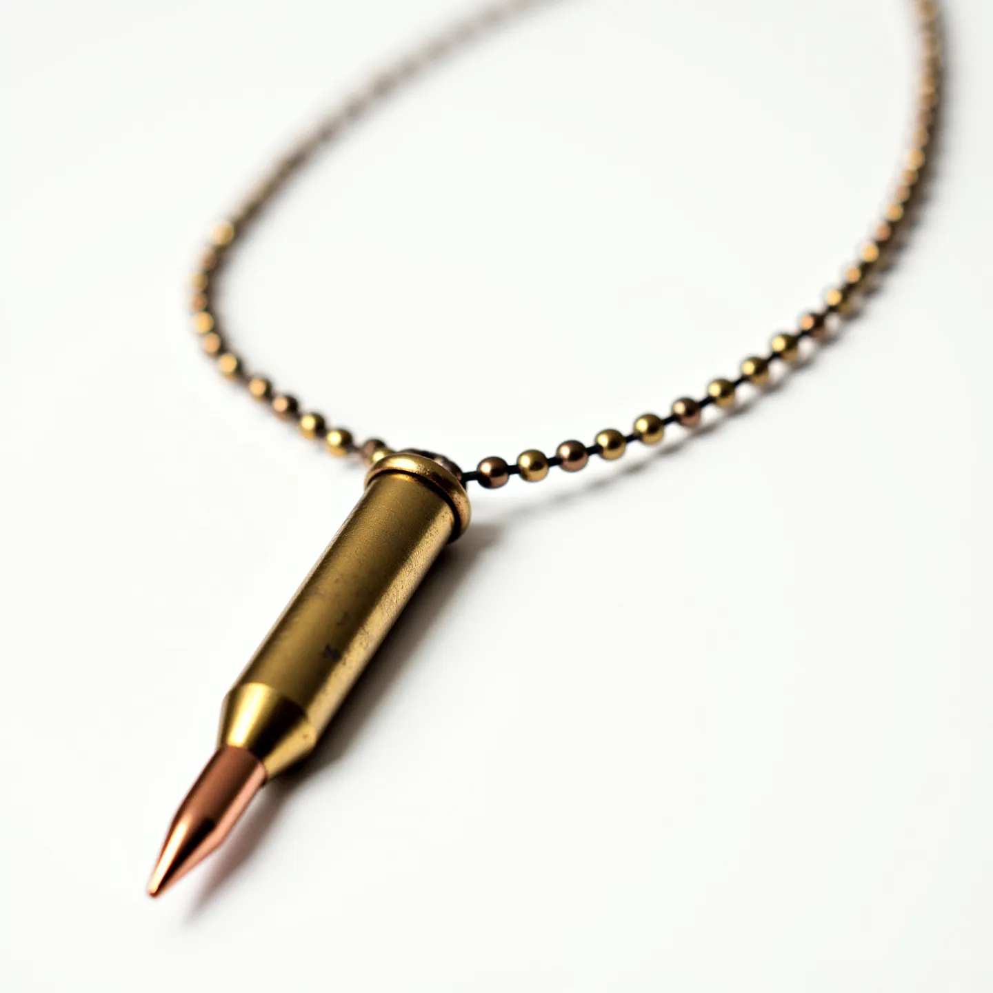 This bullet necklace features a pendant designed to resemble a bullet, with a metallic casing that exudes a brass-like appearance. The pendant is suspended from a matching round ball chain, which mirrors the metallic sheen of the bullet casing, creating a cohesive aesthetic. There are no visible gemstones on the pendant, and it is designed in a minimalist style. The chain relies on a simple connector, likely a traditional bead chain clasp, that ensures secure and easy wear. This piece combines rugged design elements with a straightforward, utilitarian form.