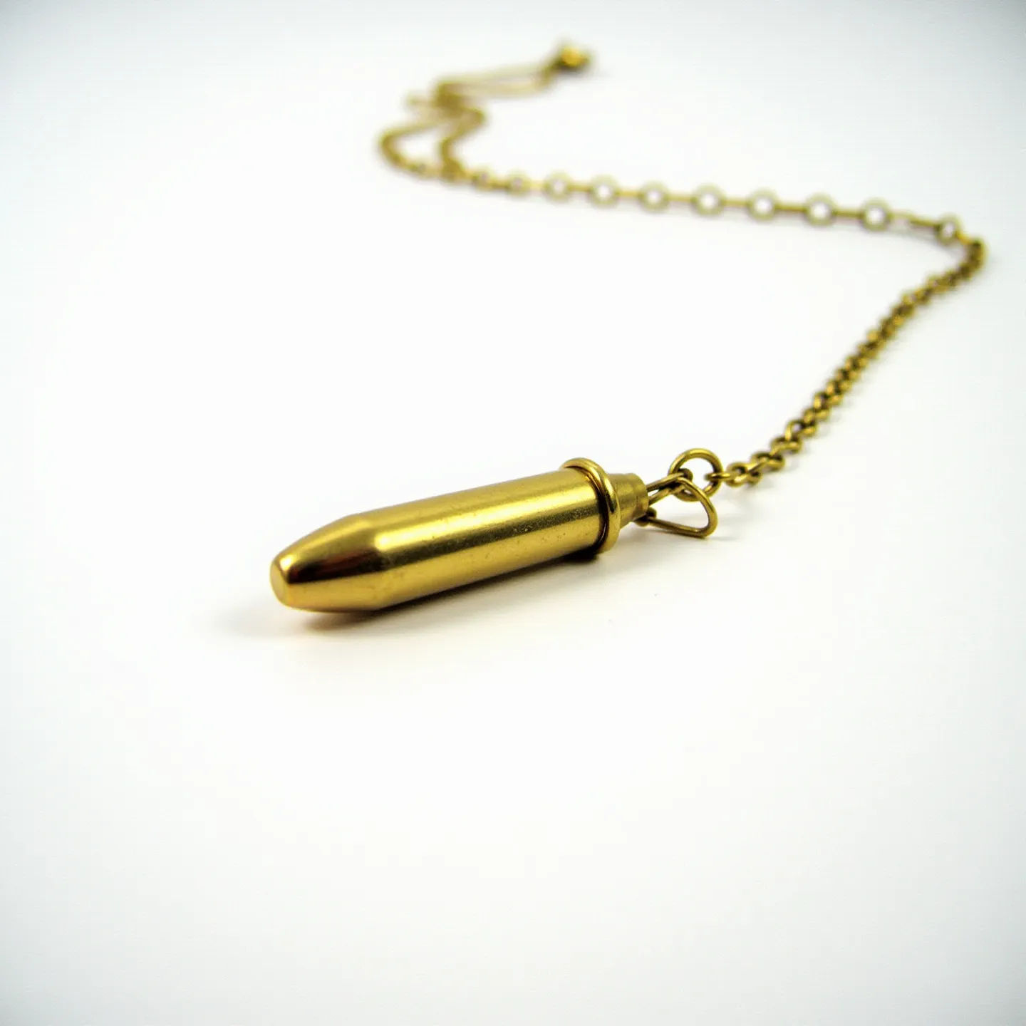 This bullet necklace features a pendant crafted from a smooth, shiny metal resembling brass, shaped authentically like a bullet. It hangs on a delicate chain, which appears to be made of a similar metallic material, providing a cohesive aesthetic. The pendant is attached to the chain via a small loop at the bullet's end, ensuring it dangles securely. This necklace emphasizes minimalistic design, focusing on the industrial appeal of the bullet form combined with the elegant simplicity of its metallic chain.